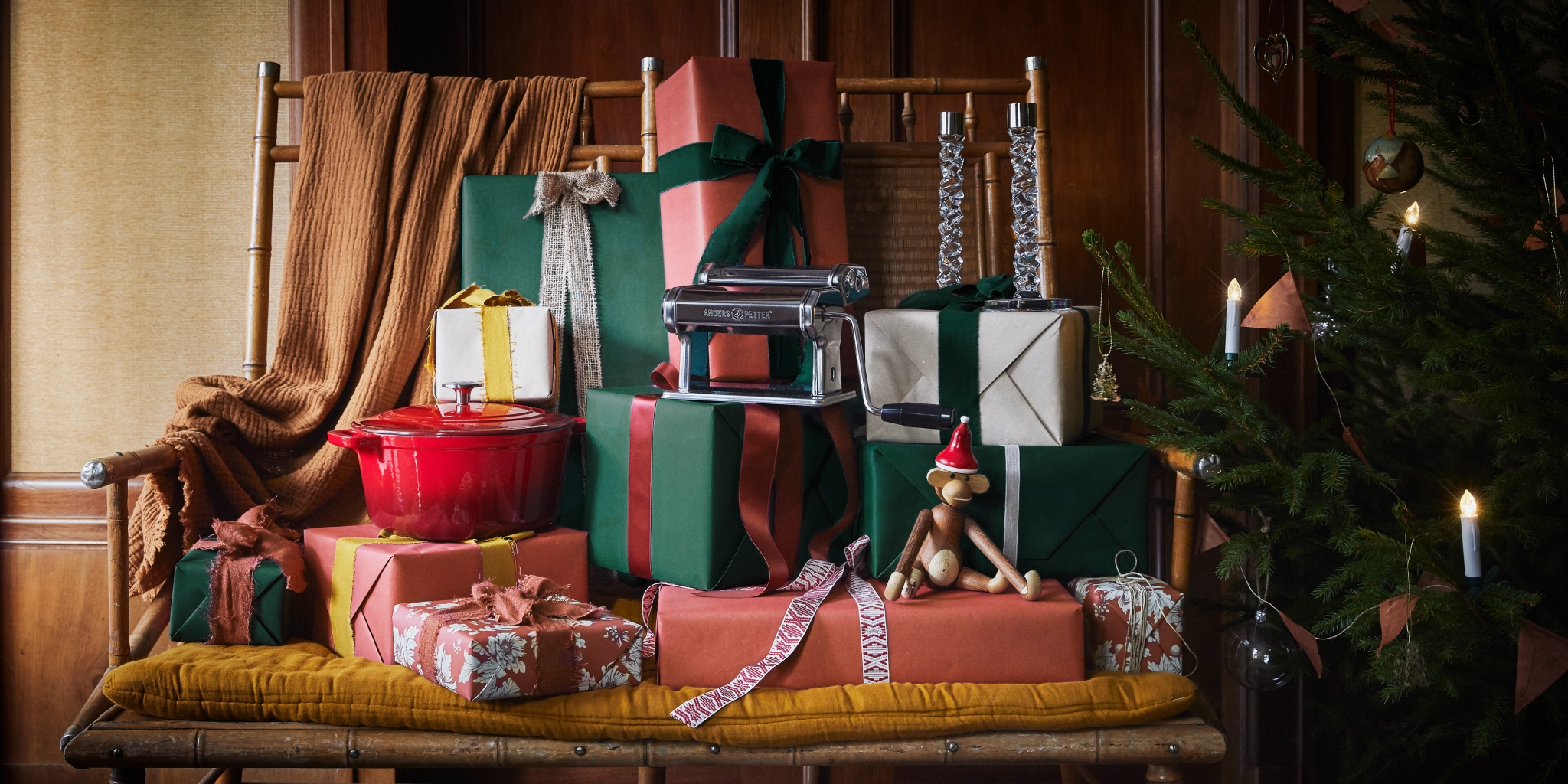 A pile of wrapped gifts, a red pot, and a pasta maker sit next to a festive Christmas tree.