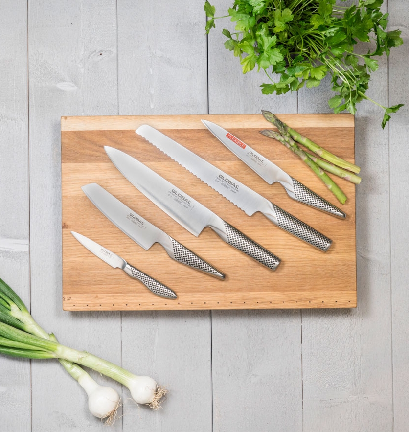 Fem knivar från Global som ligger på en skärbräda i trä