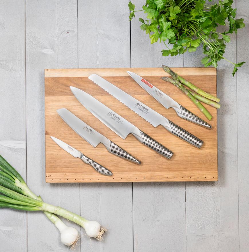 Fem knivar från Global som ligger på en skärbräda i trä