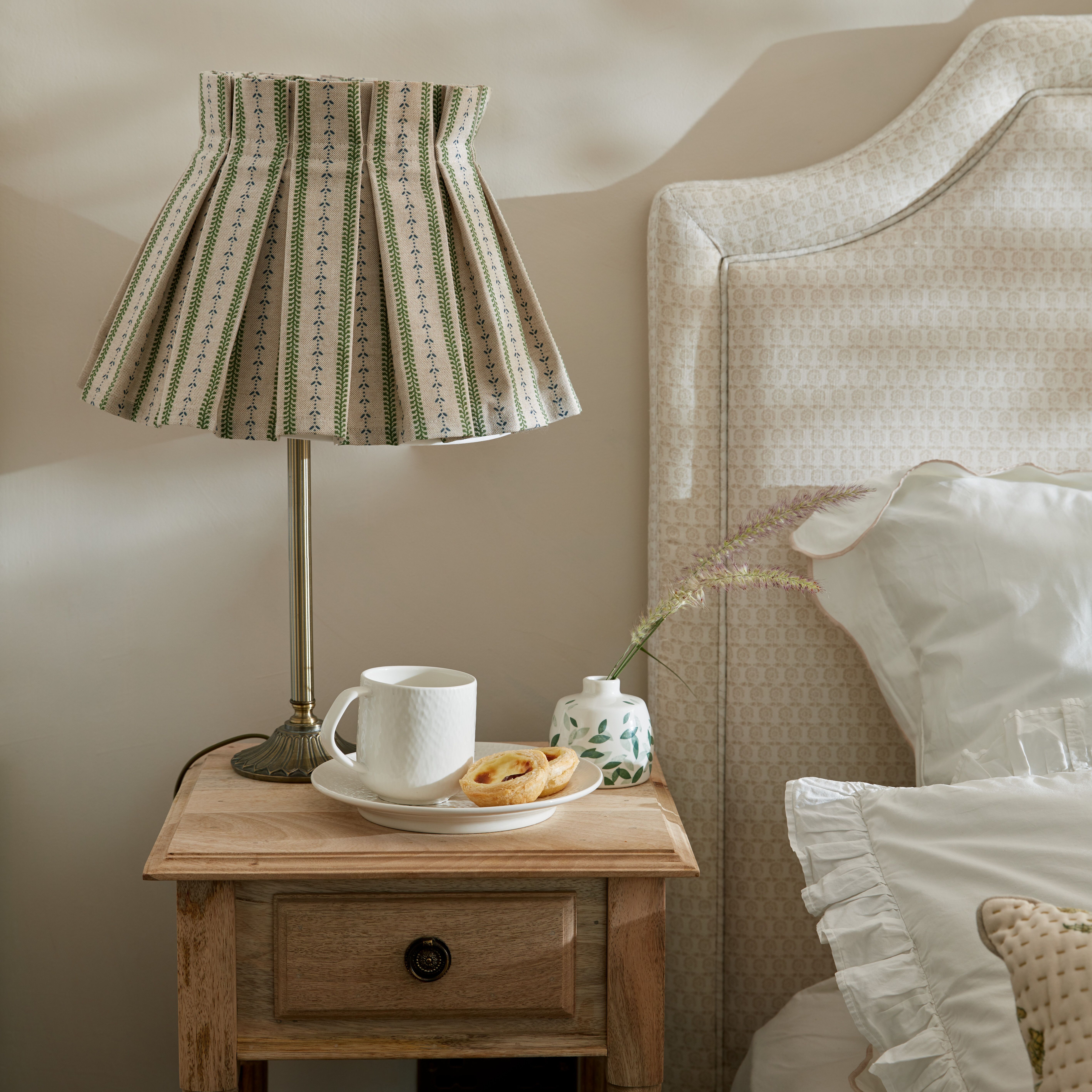 Sovrum med närbild av ett trä nattduksbord med en lampa på med randig mönstrad skärm