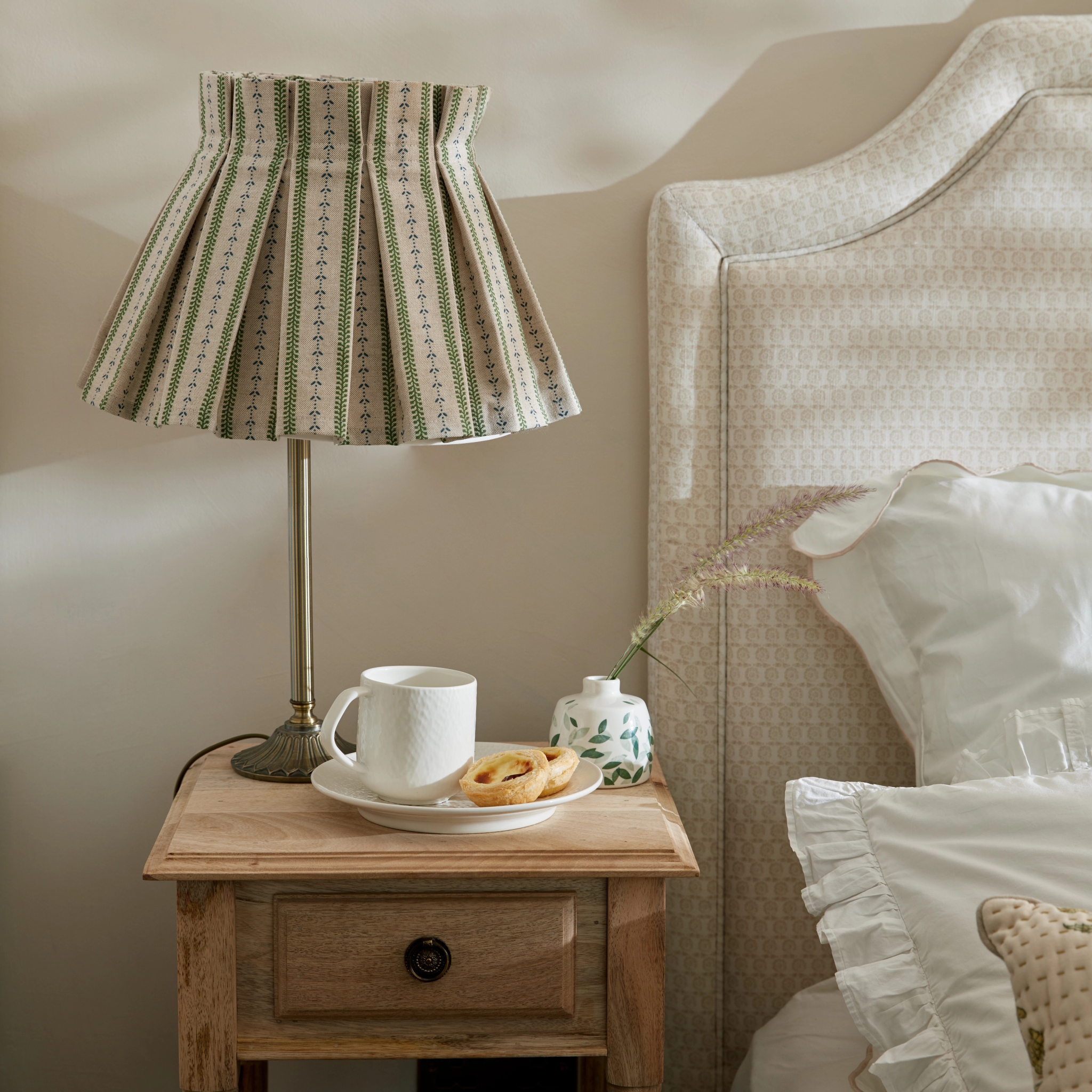 Sovrum med närbild av ett trä nattduksbord med en lampa på med randig mönstrad skärm