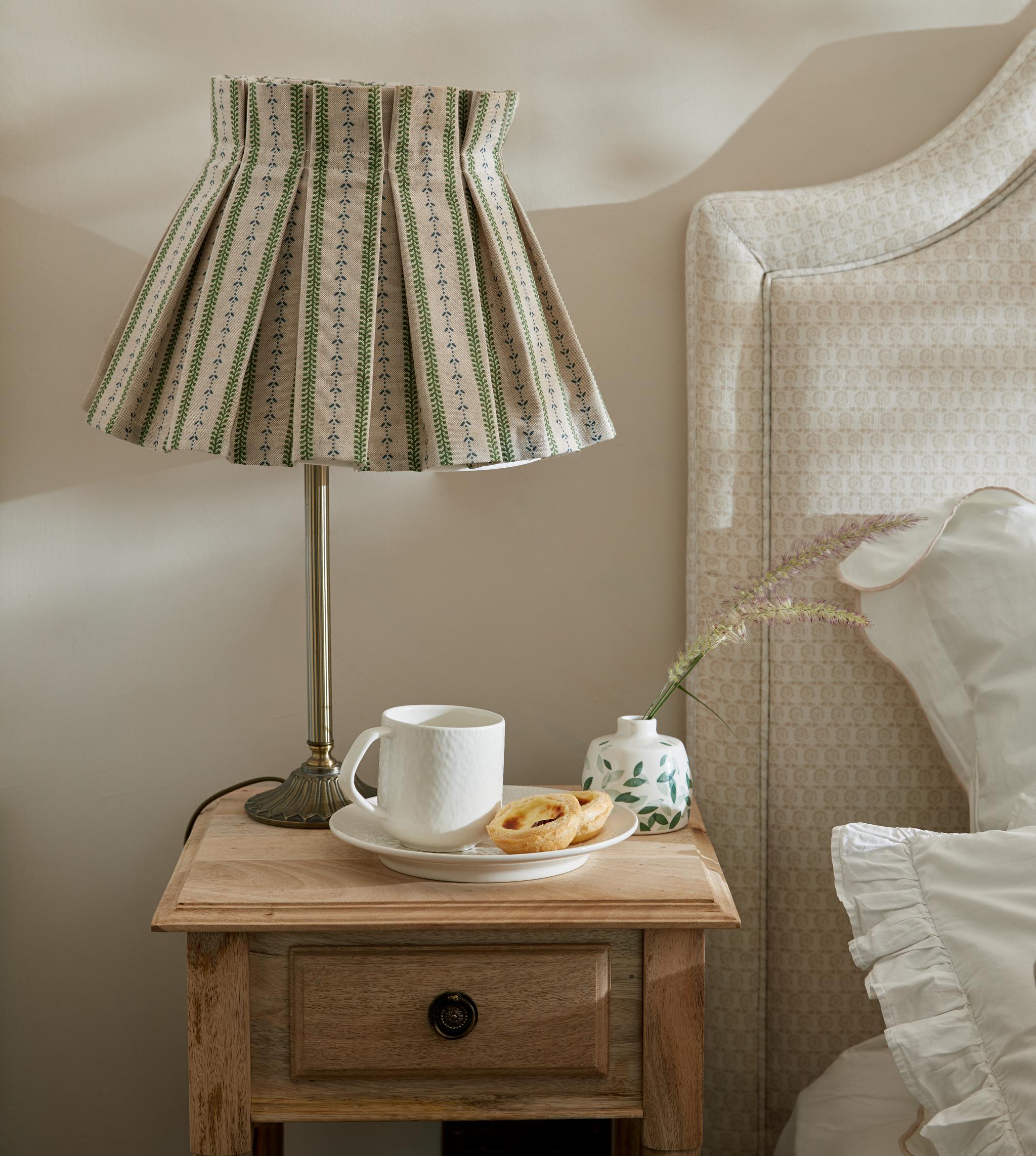 Sovrum med närbild av ett trä nattduksbord med en lampa på med randig mönstrad skärm
