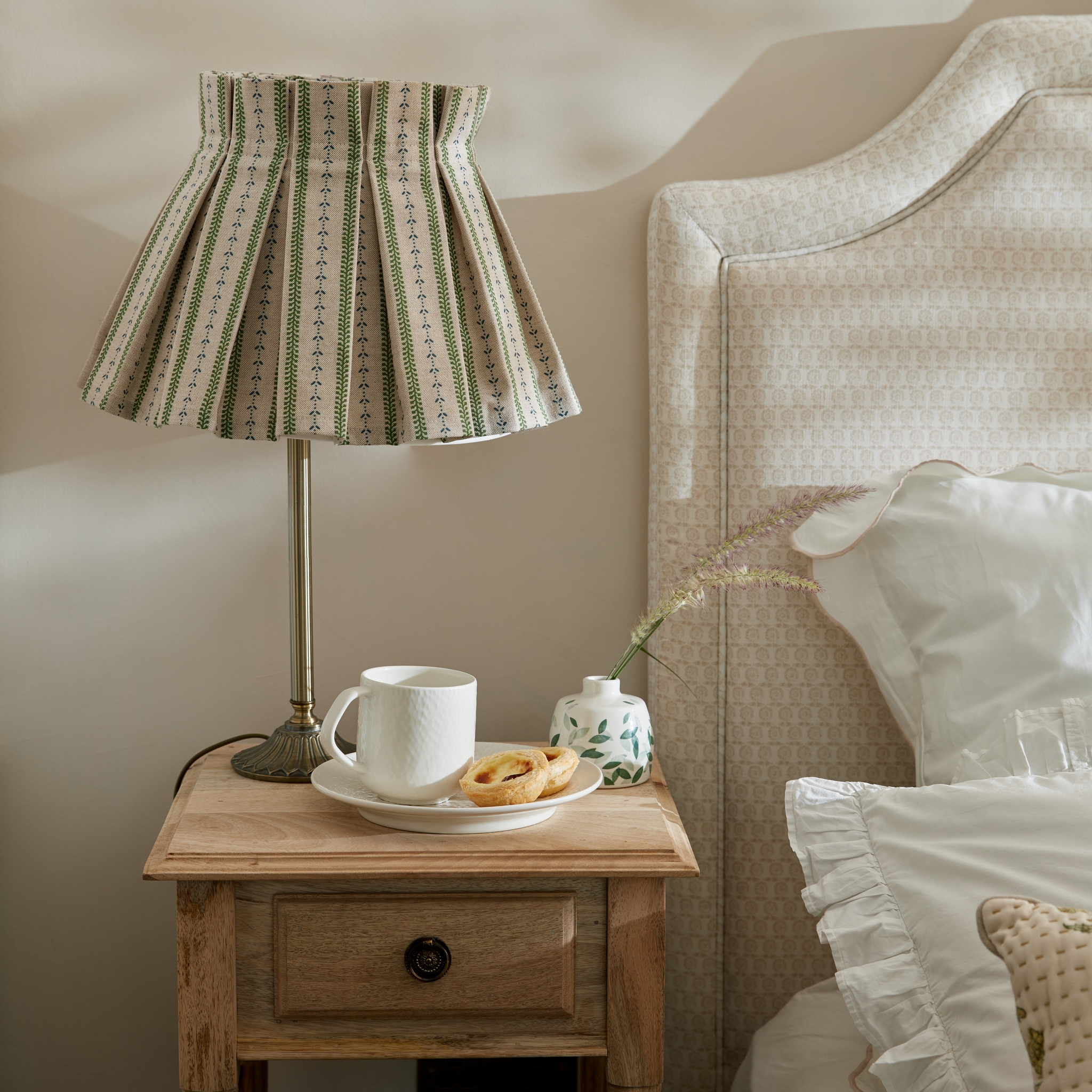 Sovrum med närbild av ett trä nattduksbord med en lampa på med randig mönstrad skärm