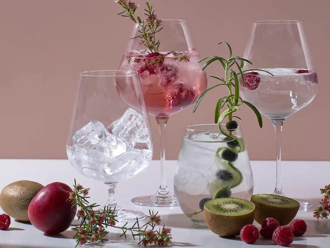 Stilfulla drinkar med is, bär, kiwi och örter uppställda på ett bord mot en rosa bakgrund.