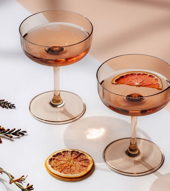 Kaksi eleganttia cocktail-lasia, joissa on roseejuomaa ja kuivattuja sitrushedelmäviipaleita.