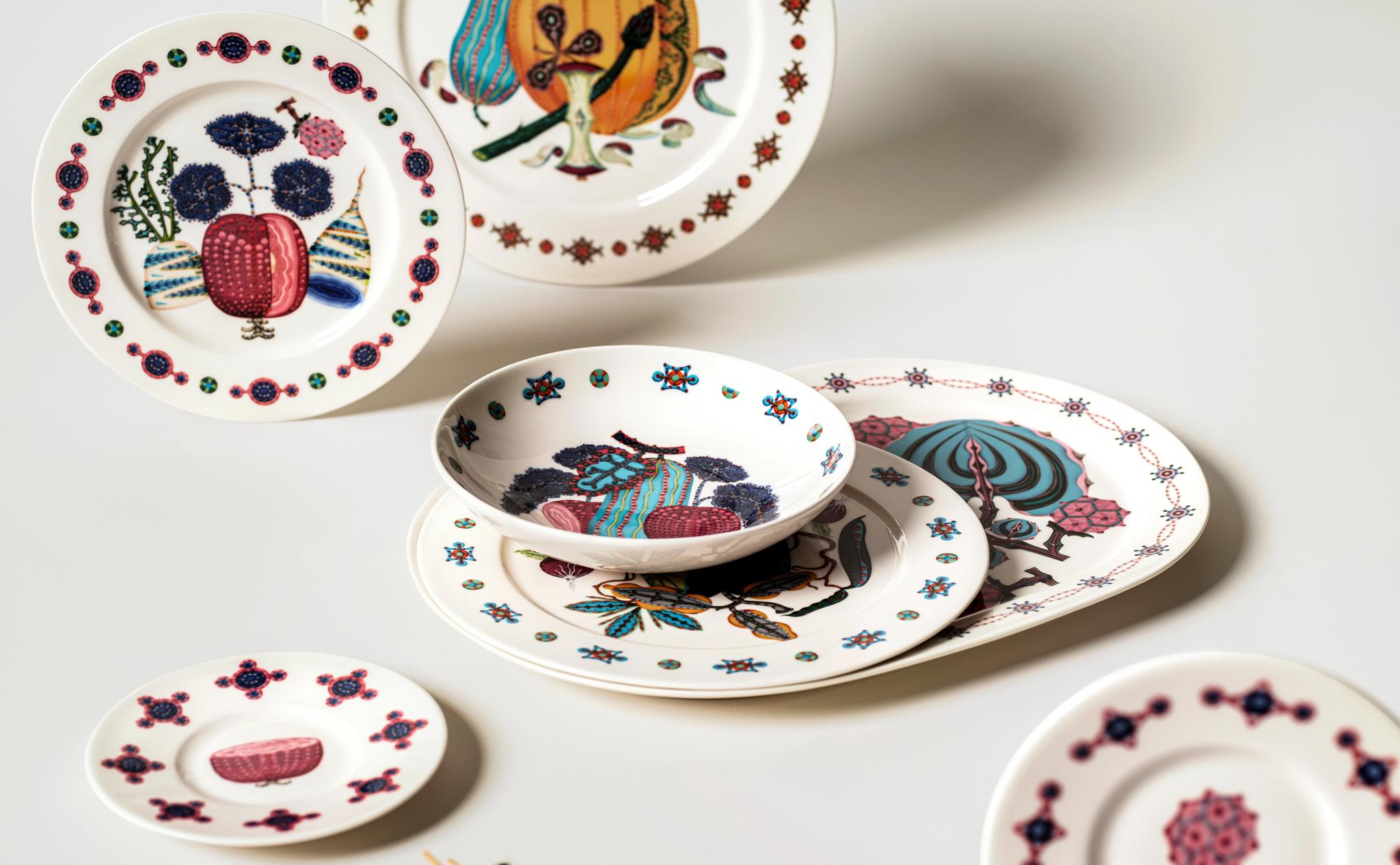 Värikkäästi kuvioidut design-lautaset ja kulhot on aseteltu vaalealle pöydälle tyylikkääseen kattaukseen.