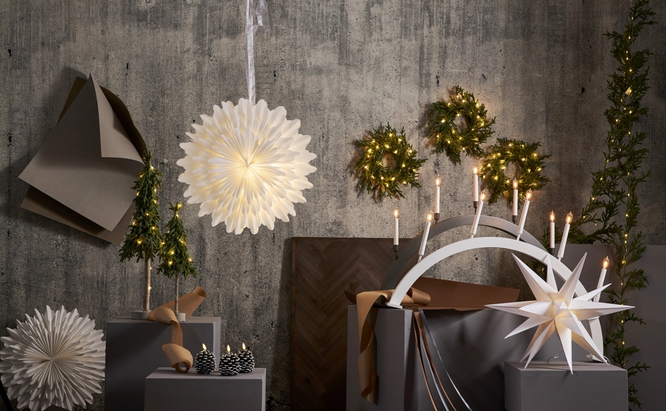 Scandinavian-style Christmas decorations featuring illuminated paper stars, mini trees, wreaths, and an arched candelabra.