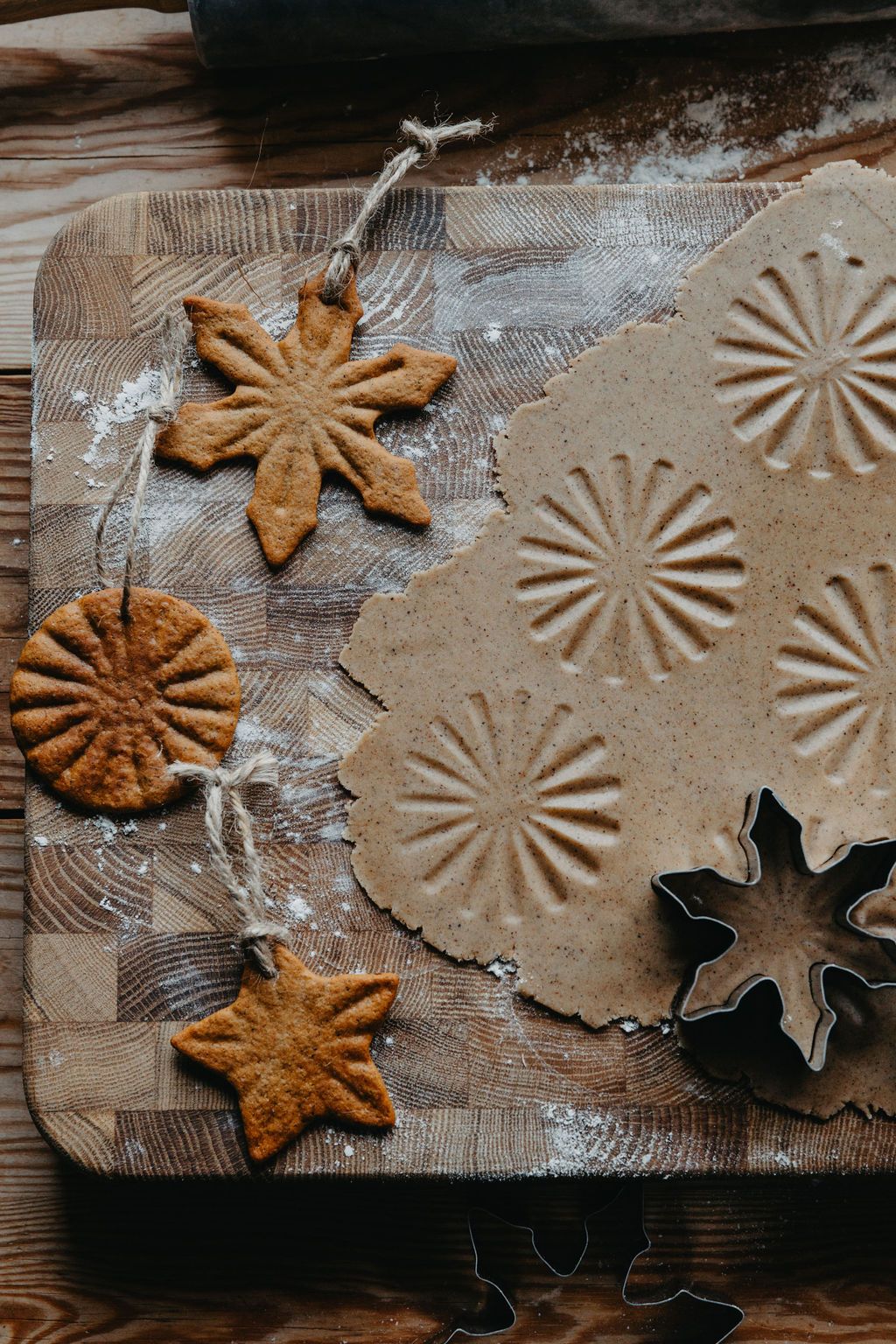 Pepparkaksdeg med präglade mönster, bakade snöflingor, stjärnor och runda kakor med snöre och kakformar på en mjölad träbräda.
