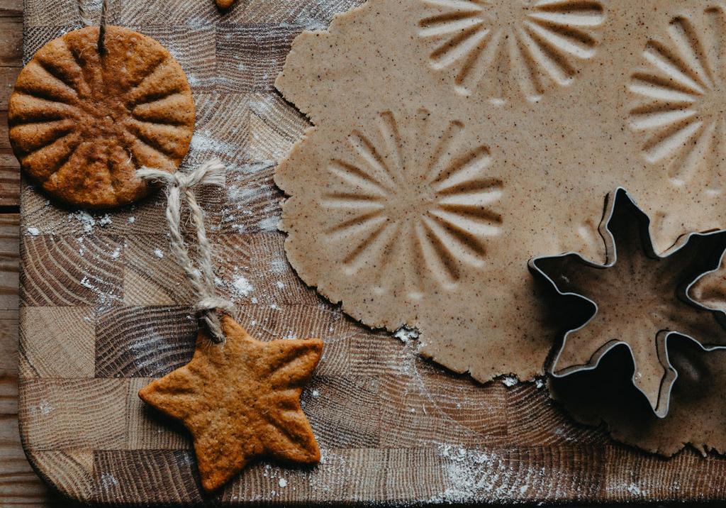 Pepparkaksdeg med präglade mönster, bakade snöflingor, stjärnor och runda kakor med snöre och kakformar på en mjölad träbräda.