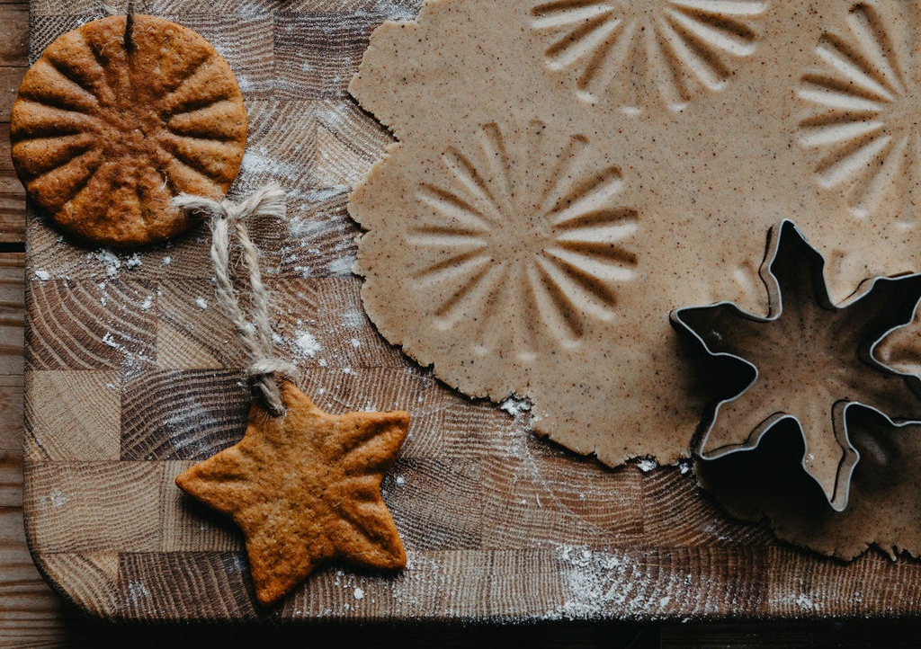 Pepparkaksdeg med präglade mönster, bakade snöflingor, stjärnor och runda kakor med snöre och kakformar på en mjölad träbräda.