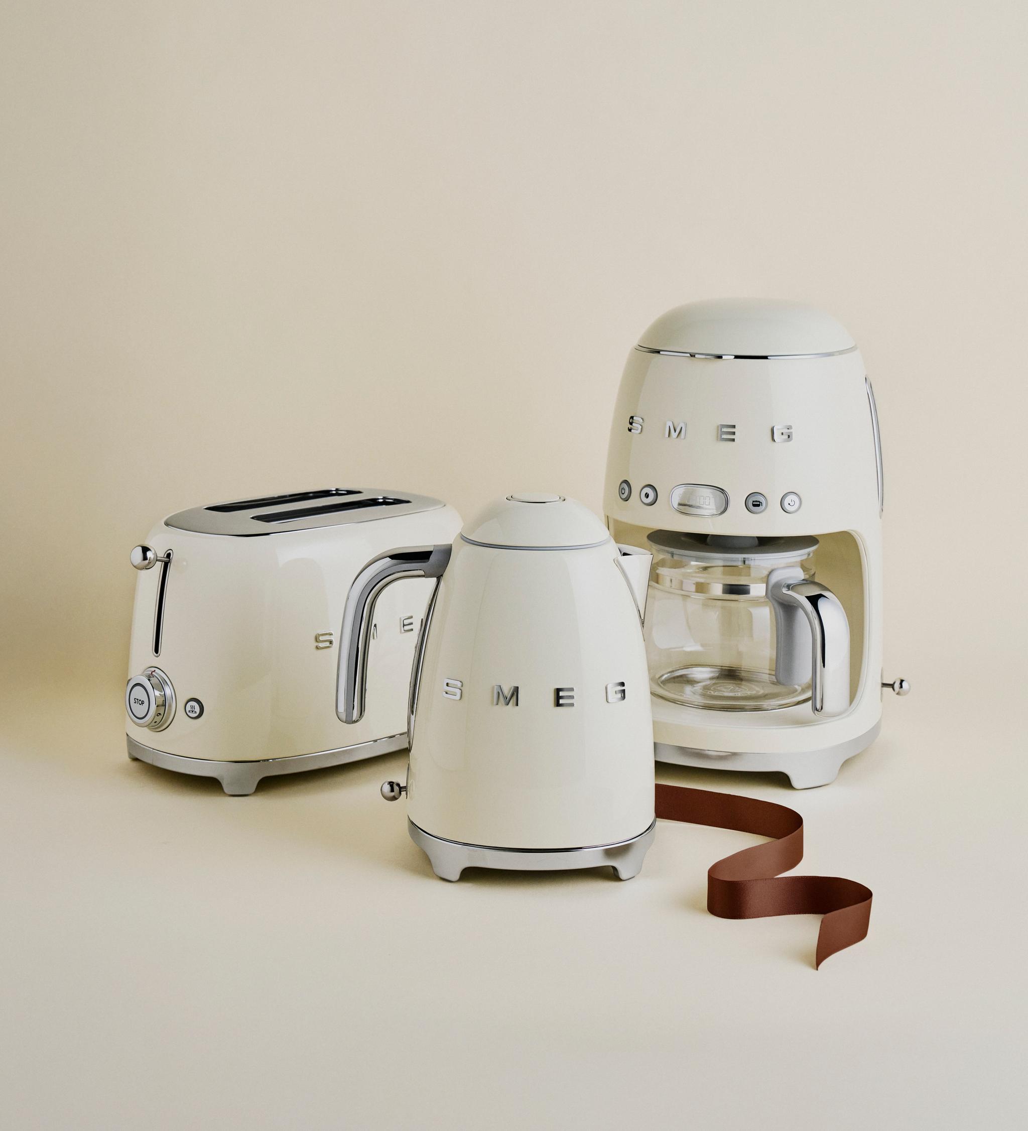 Krämfärgade SMEG köksapparater – brödrost, vattenkokare och kaffebryggare – står uppställda mot en beige bakgrund.