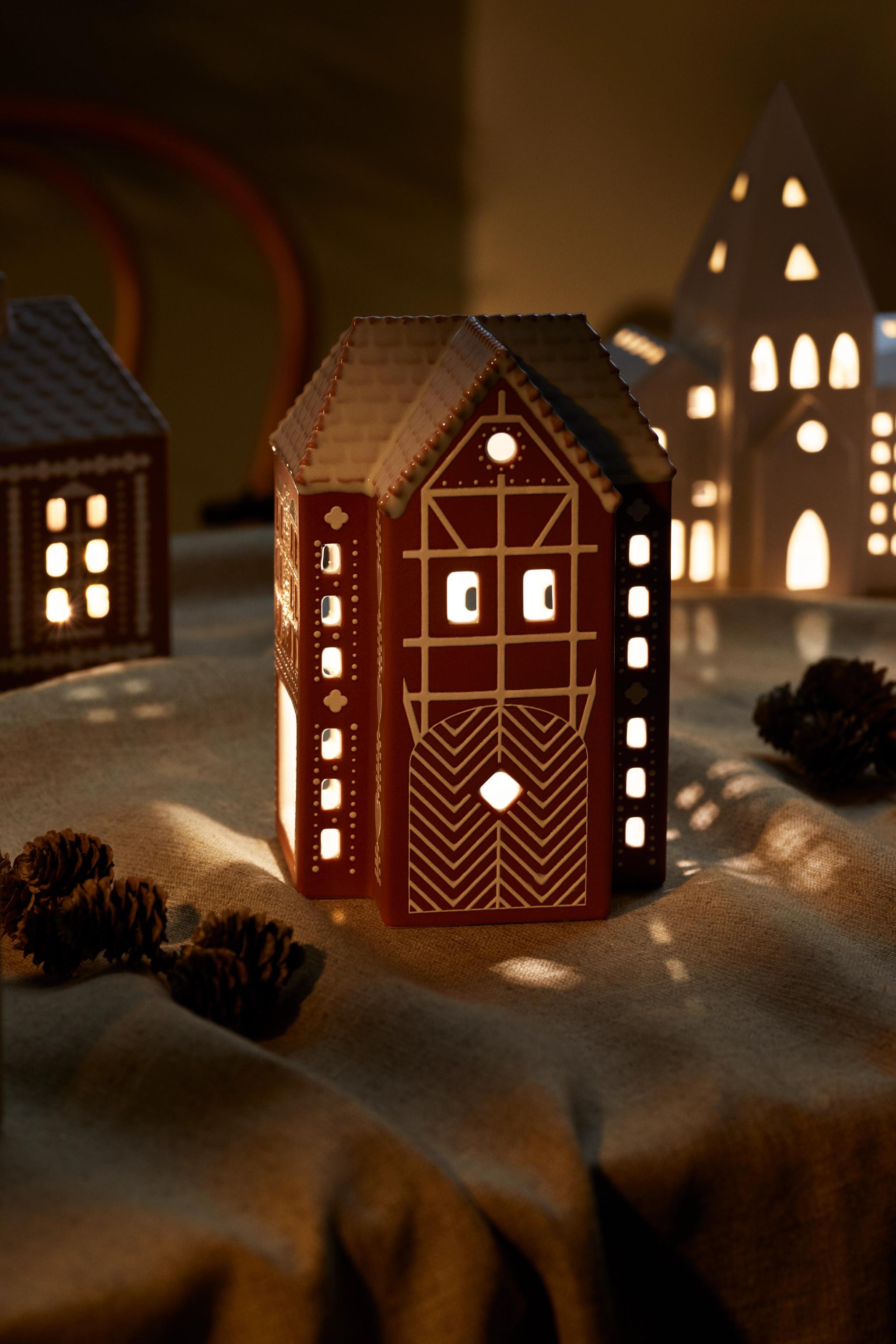 En ljuslykta som ser ut som ett pepparkakshus är tänd på ett bord