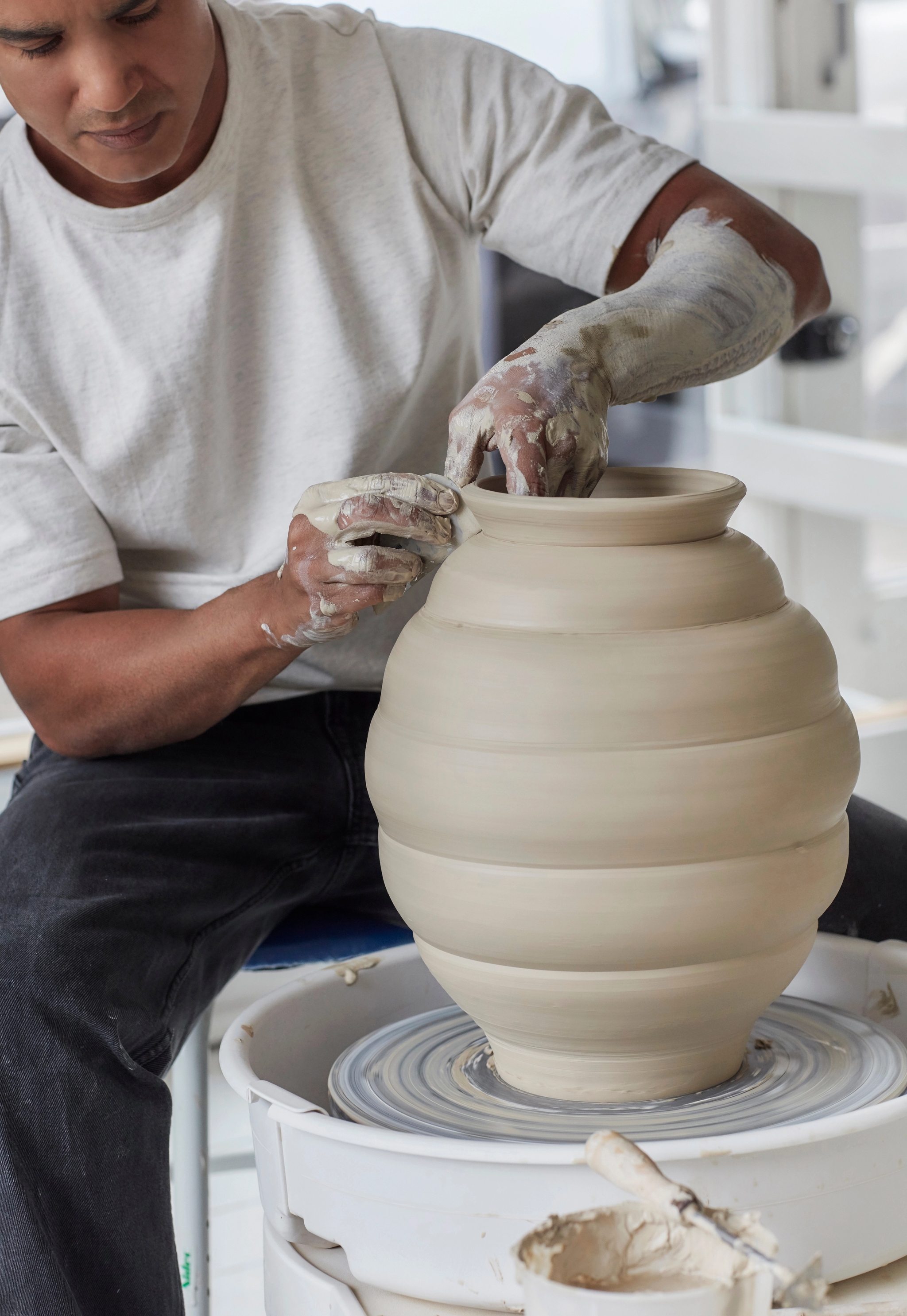 A potter shaping a large, ribbed clay vase on a pottery wheel.