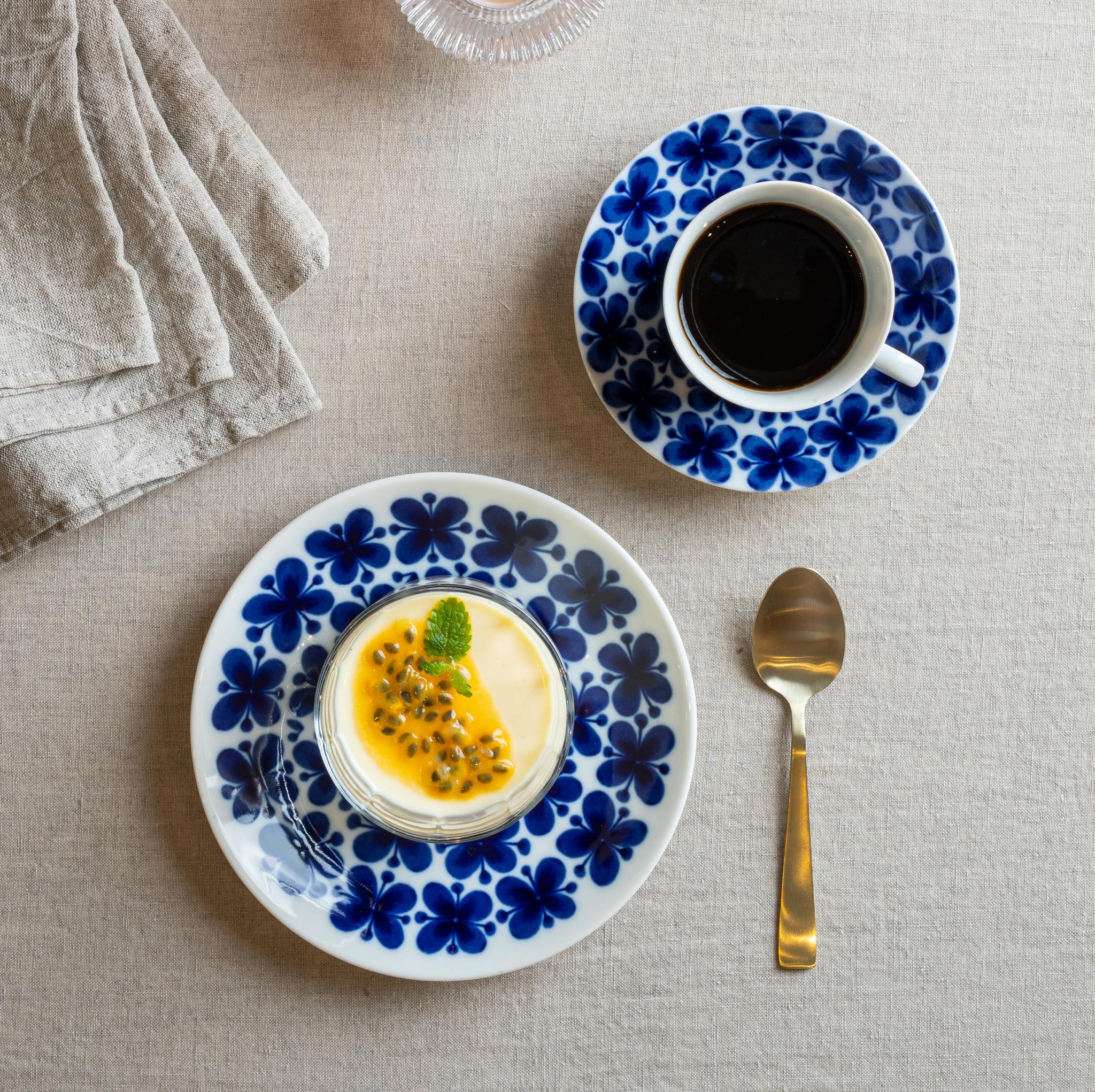 Dukat fikabord med kaffe, passionsfruktsdessert, levande ljus och blåblommigt porslin på en linneduk.