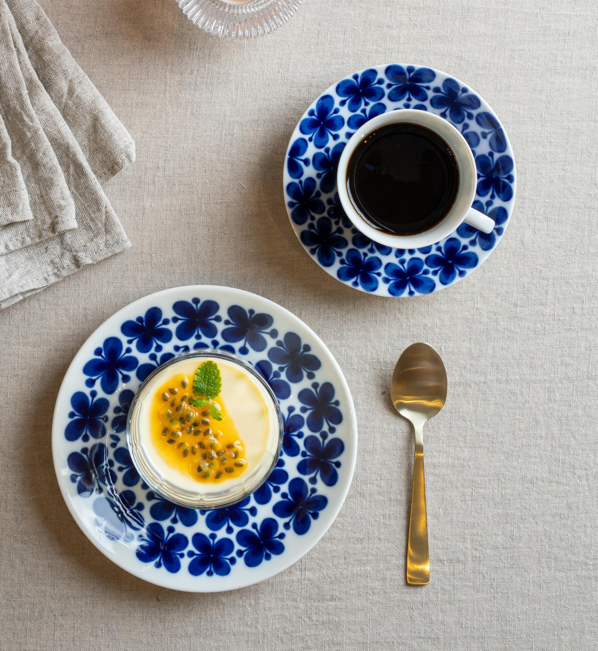 Dessert med pasjonsfrukt og kaffe på blåblomstret servise, omgitt av levende lys og tørkede blomster.