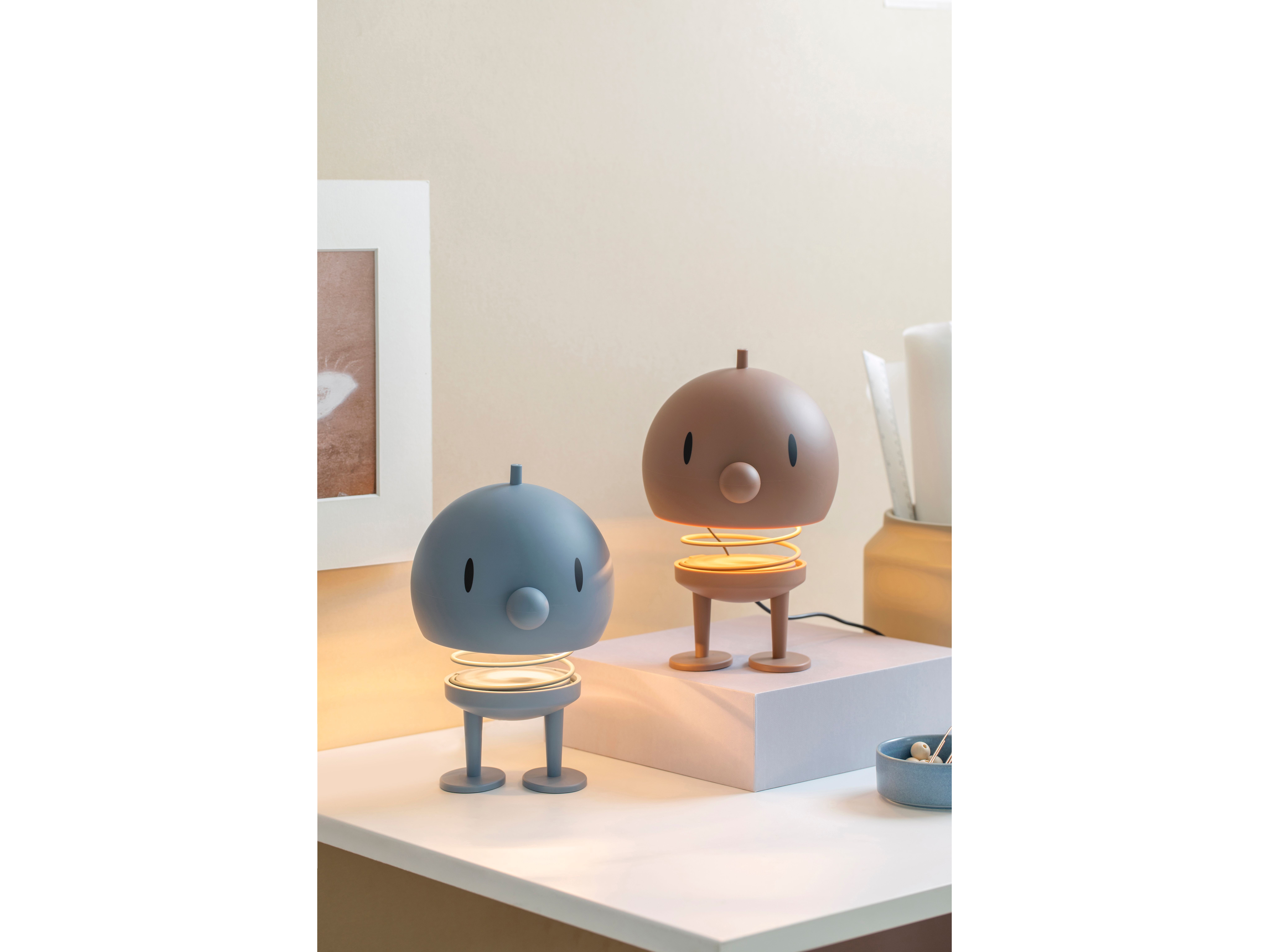 På ett vitt skrivbort står två Hoptimist lampor i färgerna blått och brunt