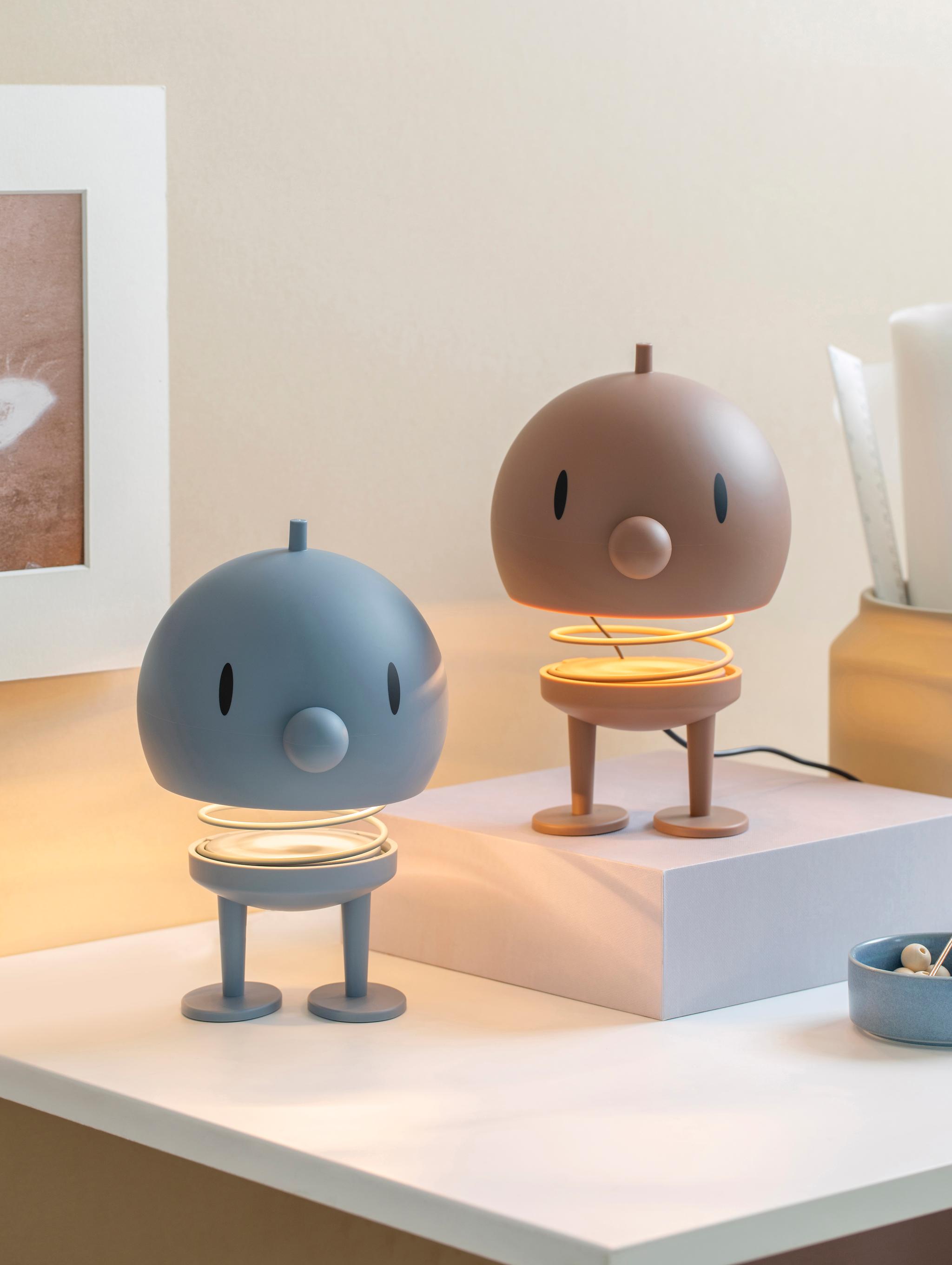 På ett vitt skrivbort står två Hoptimist lampor i färgerna blått och brunt