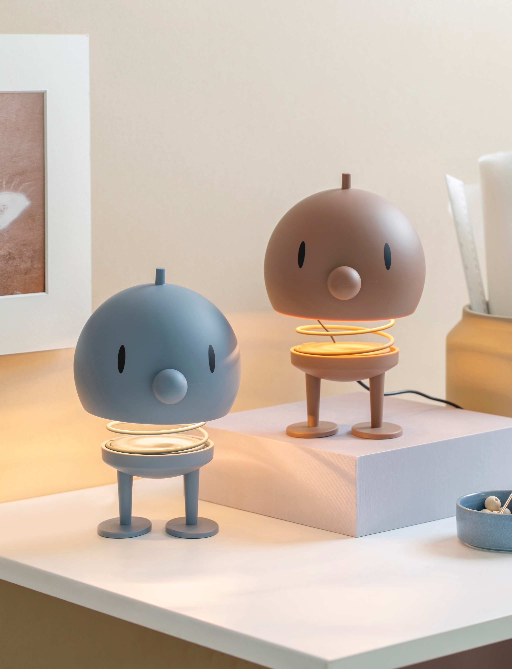 På ett vitt skrivbort står två Hoptimist lampor i färgerna blått och brunt