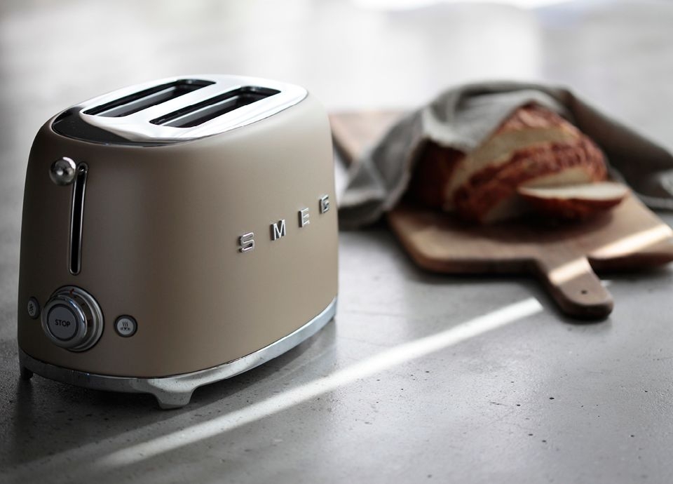 Smeg brödrost i matt guld med rostat bröd på en skärbräda