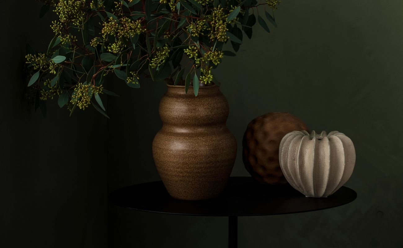 Vaser i jordnära färger mot en mörkgrön bakgrund