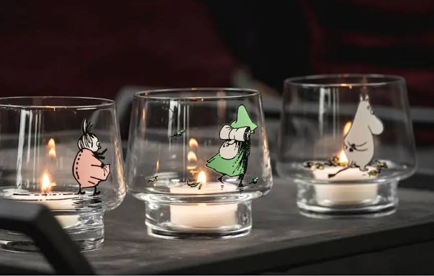 Kolme lasista Muurla kynttilälyhtyä, joissa on Muumi-hahmoja ja palavat kynttilät