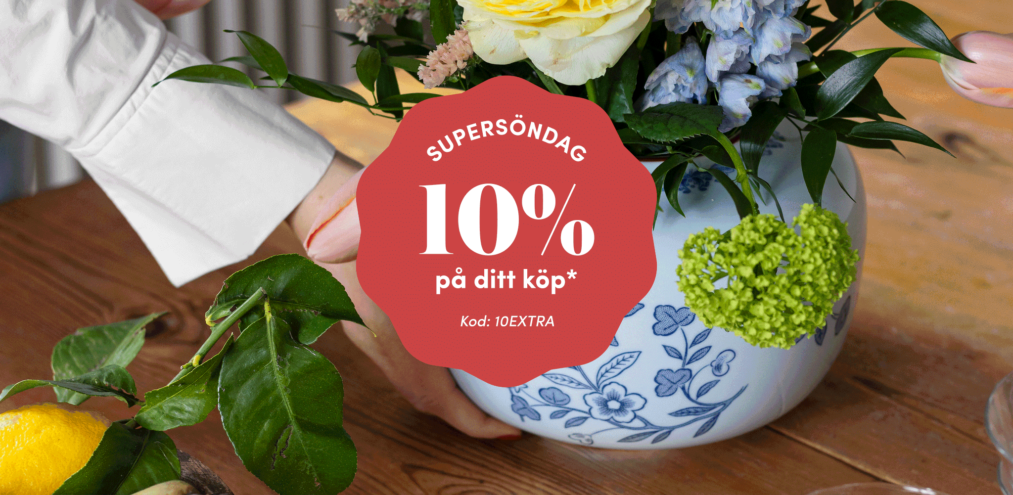 Hands holding a vase of colorful flowers, overlaid with a red banner stating "SUPERSÖNDAG 10% på ditt köp* Kod: 10EXTRA".