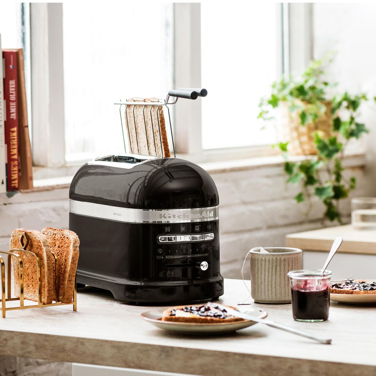Tyylikäs musta KitchenAid-leivänpaahdin modernilla keittiön tasolla paahtoleivän, hillon ja teen kanssa.