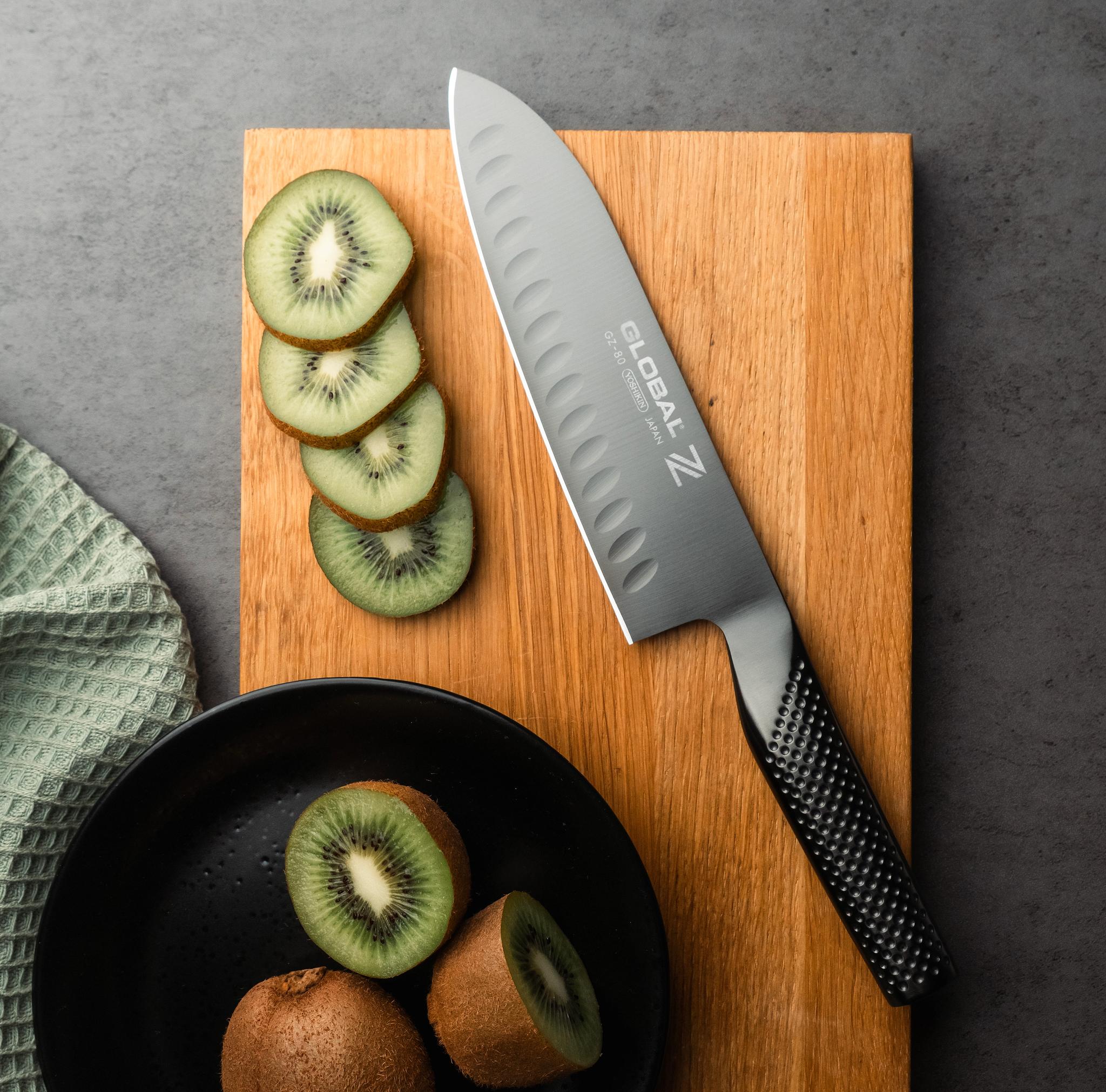 Oppskåret kiwi og en Global-kokkekniv på et skjærebrett av tre.