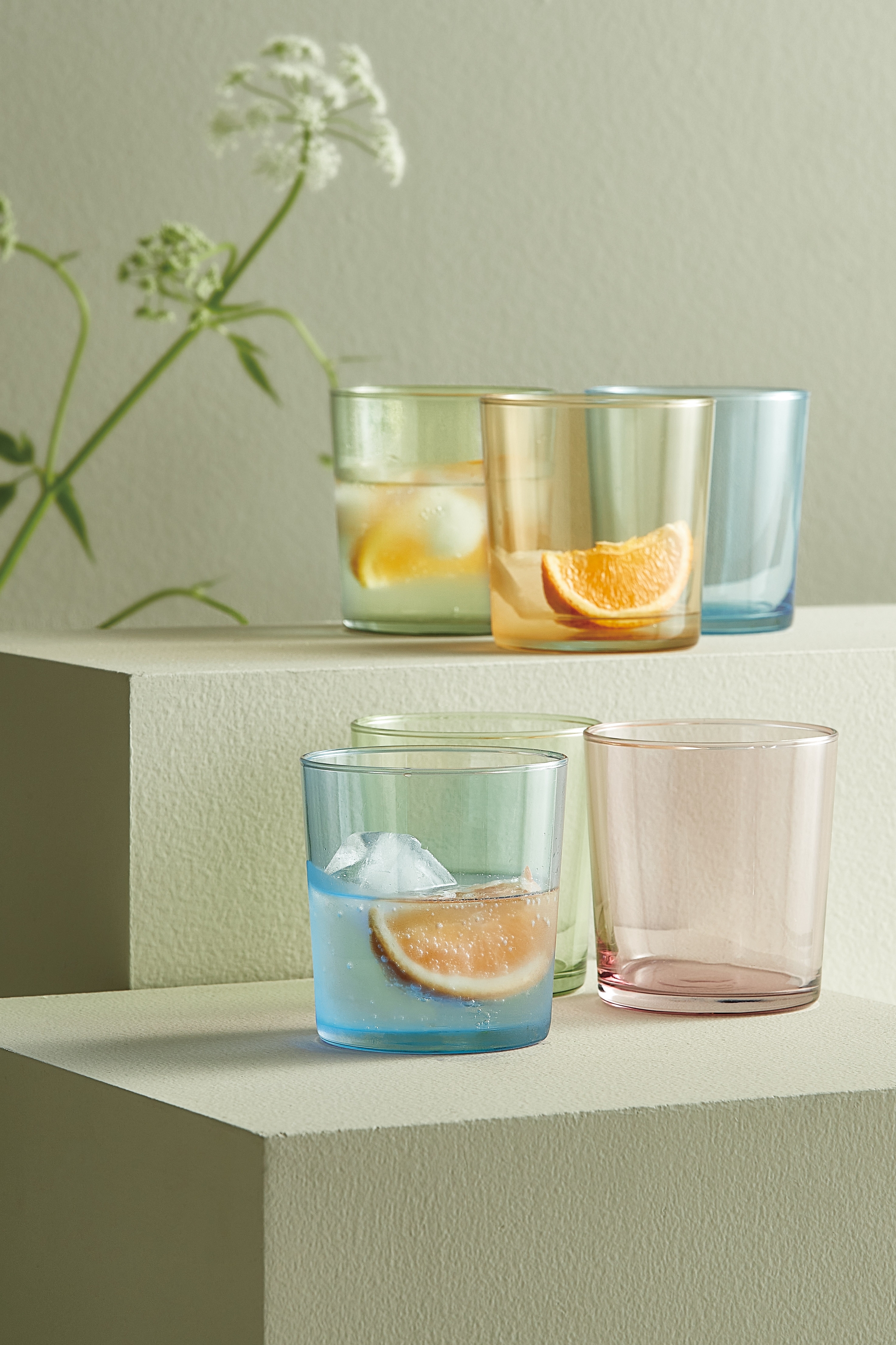four different colored glasses with ice and a slice of orange in them