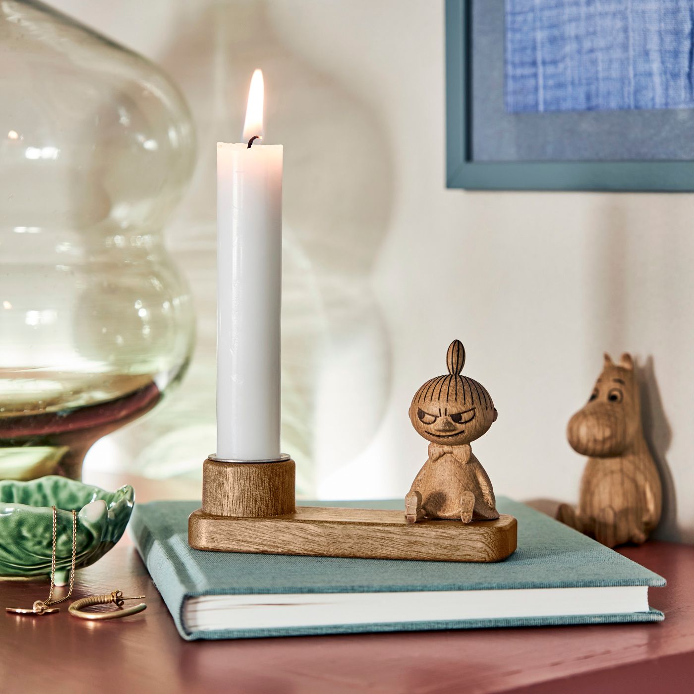 Träljusstake med Mumin-figur och tänt vitt stearinljus på en bok i en hemtrevlig inredning.