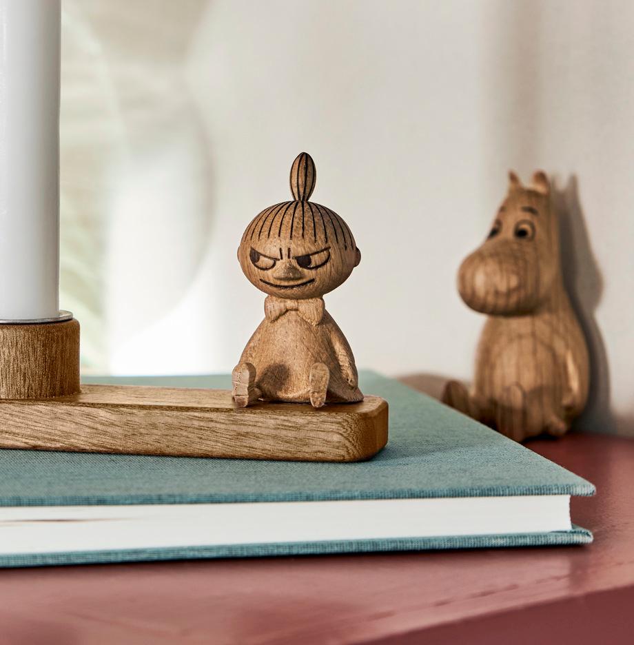 Träljusstake med Mumin-figur och tänt vitt stearinljus på en bok i en hemtrevlig inredning.