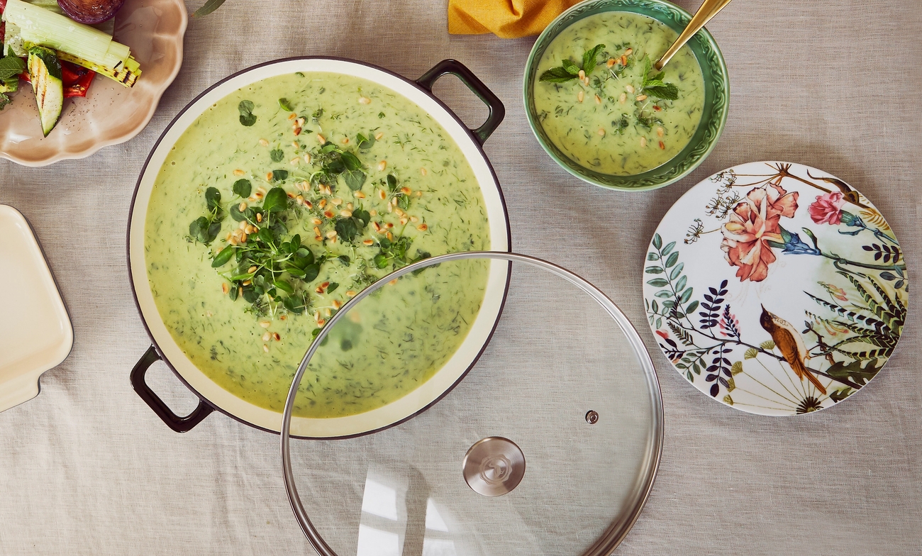 Ylhäältä päin kuvattu ruokapöytä, jossa on suuri kattilallinen viherkeittoa, grillattuja kasviksia ja paahdettua parsakaalia.