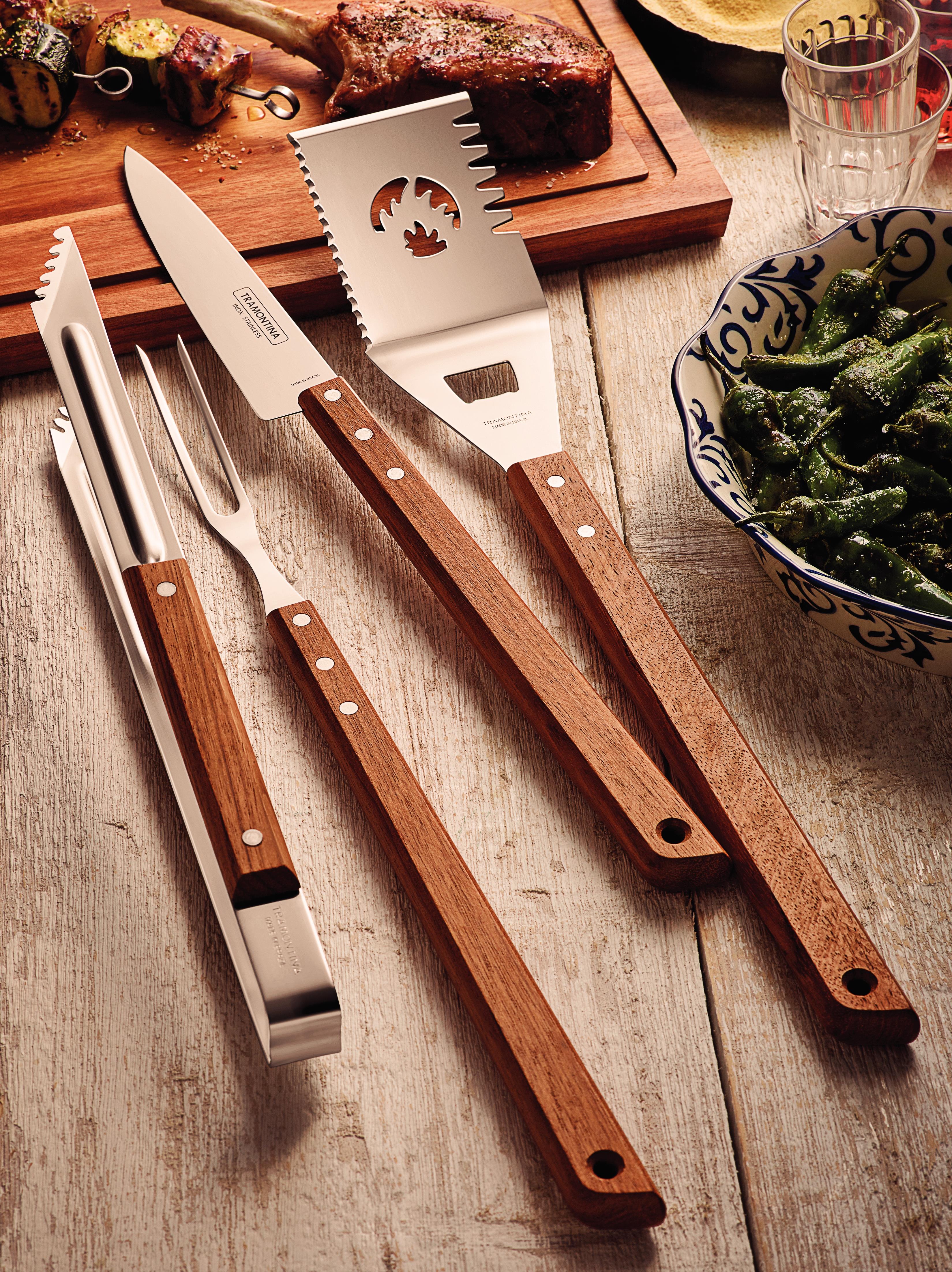 Grillverktyg med trähandtag bredvid grillat kött och paprika på ett träbord.