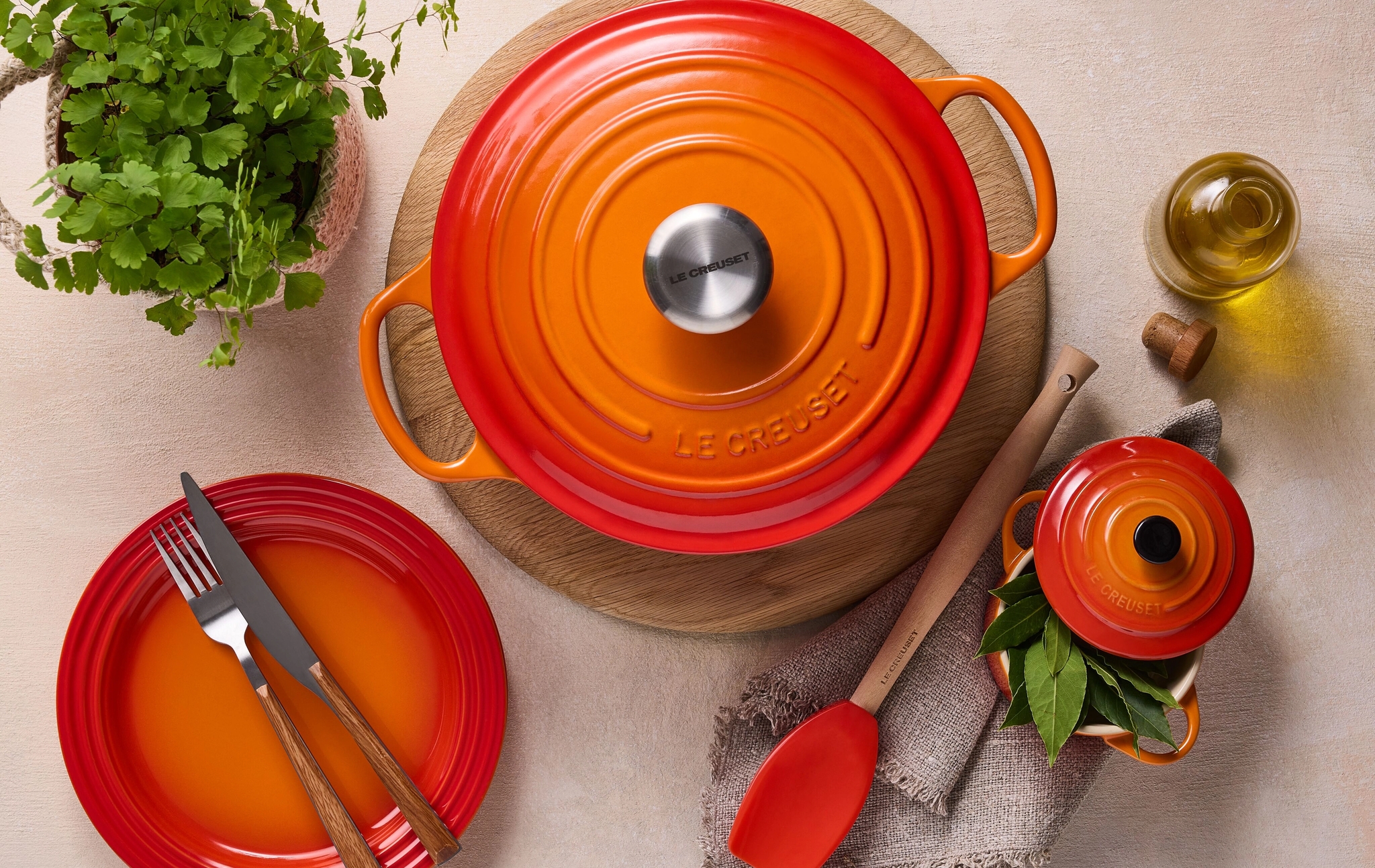 Värikäs Le Creuset -valurautapata ja lautanen kattauksessa yrttien ja oliiviöljyn kanssa keittiön pöydällä.