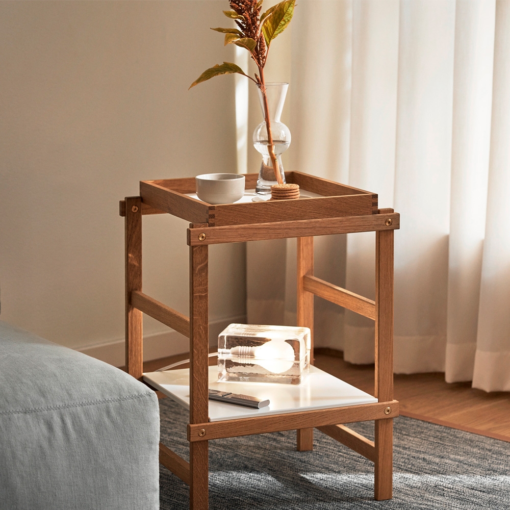 Kaksikerroksinen puinen sivupöytä, jonka päällä on maljakko ja kulho sekä alimmalla hyllyllä ainutlaatuinen kirkas pöytävalaisin.