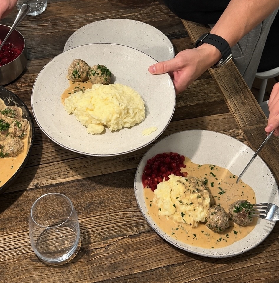 Person serverar svenska köttbullar med potatismos, gräddsås och lingon på ett rustikt träbord.