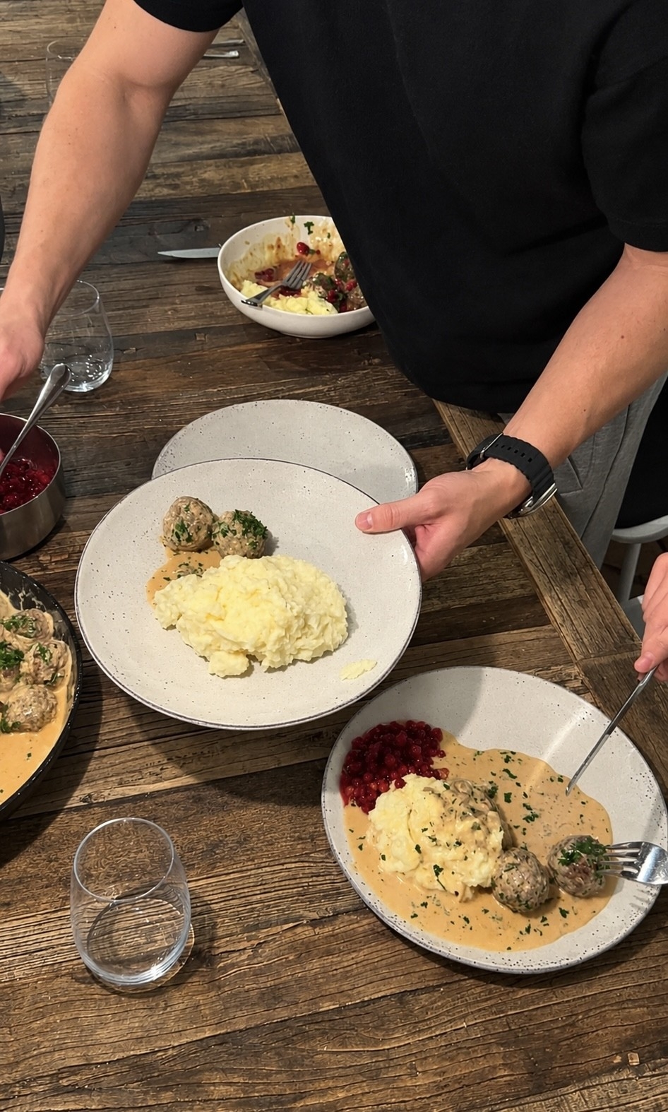 Person serverar svenska köttbullar med potatismos, gräddsås och lingon på ett rustikt träbord.