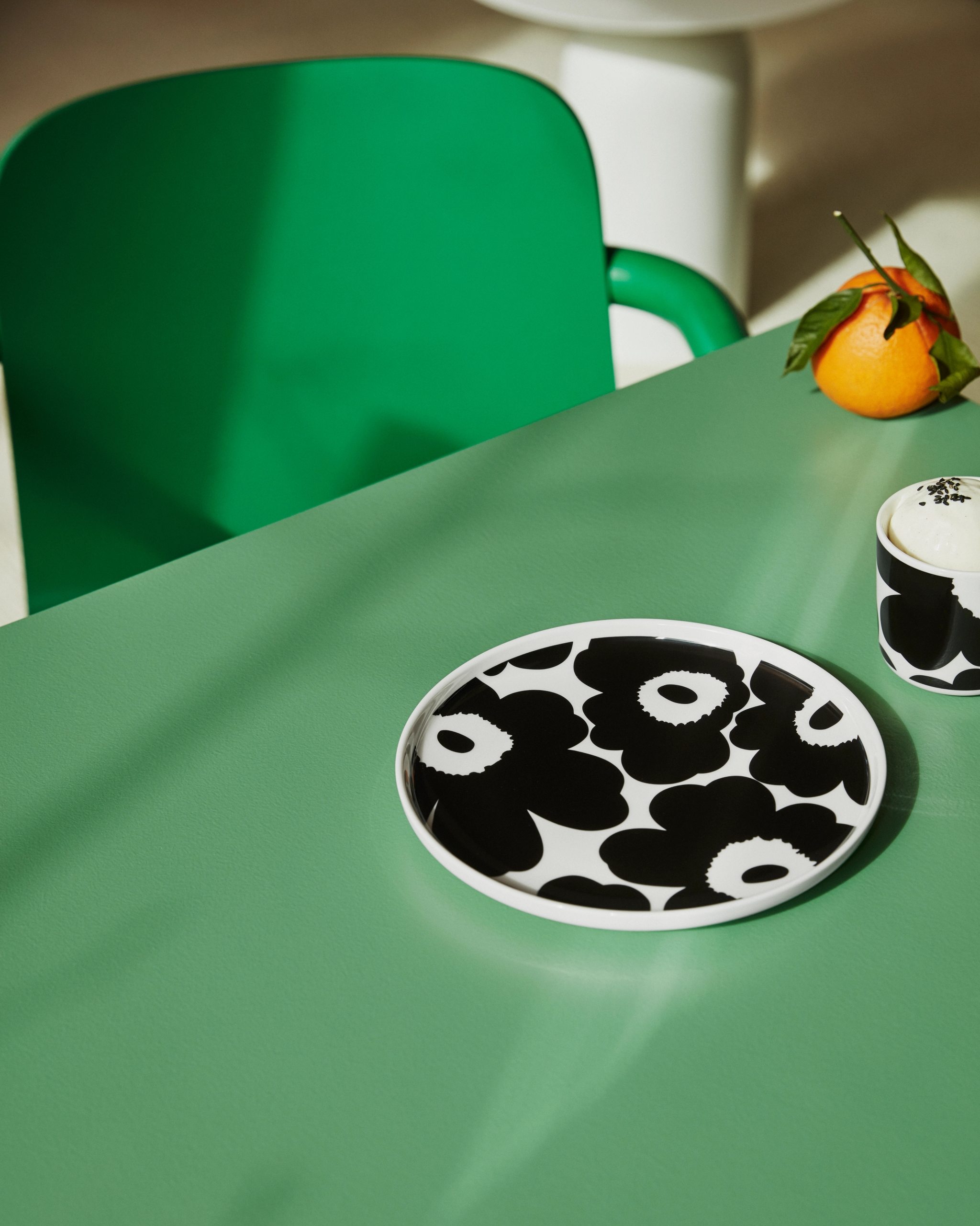 Mustavalkoinen Marimekko unikko lautanen ja muki vihreällä pöydällä 