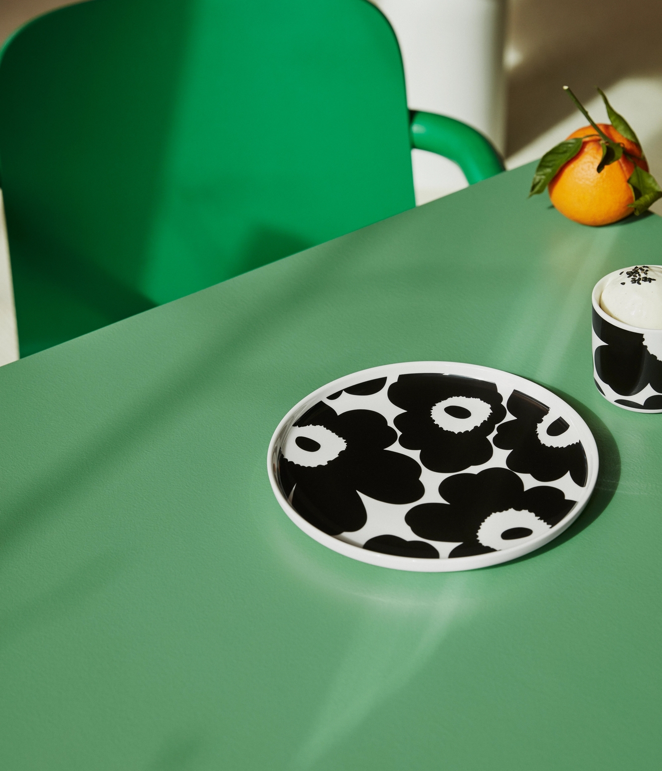 Mustavalkoinen Marimekko unikko lautanen ja muki vihreällä pöydällä