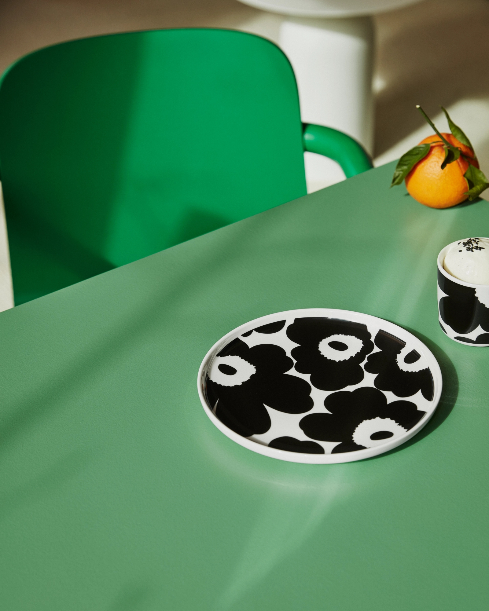 Mustavalkoinen Marimekko unikko lautanen ja muki vihreällä pöydällä