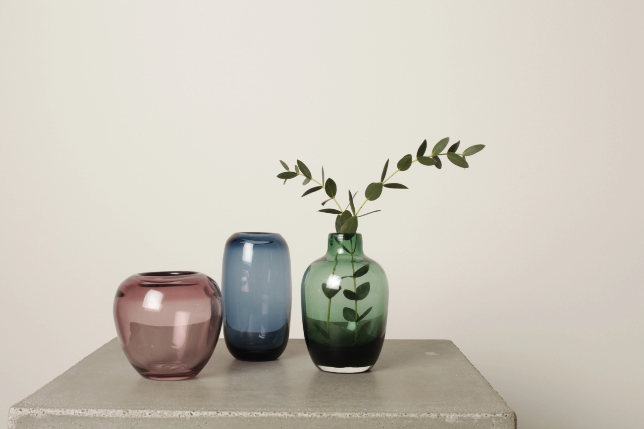 Kolme pientä maljakkoa väreissä ruskea, sininen ja vihreä petonipöydällä harmaalla taustalla