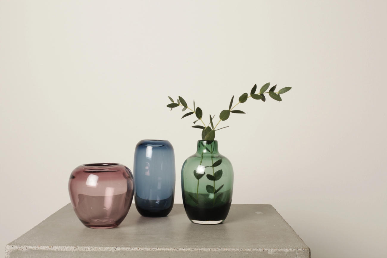 Kolme pientä maljakkoa väreissä ruskea, sininen ja vihreä petonipöydällä harmaalla taustalla