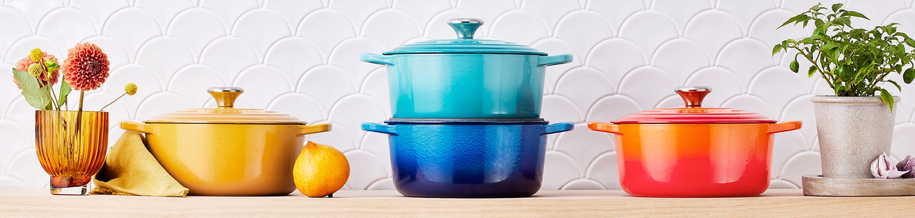 Le Creuset gjutjärnsgrytor i regnbågens alla färger på en hylla i ett kök