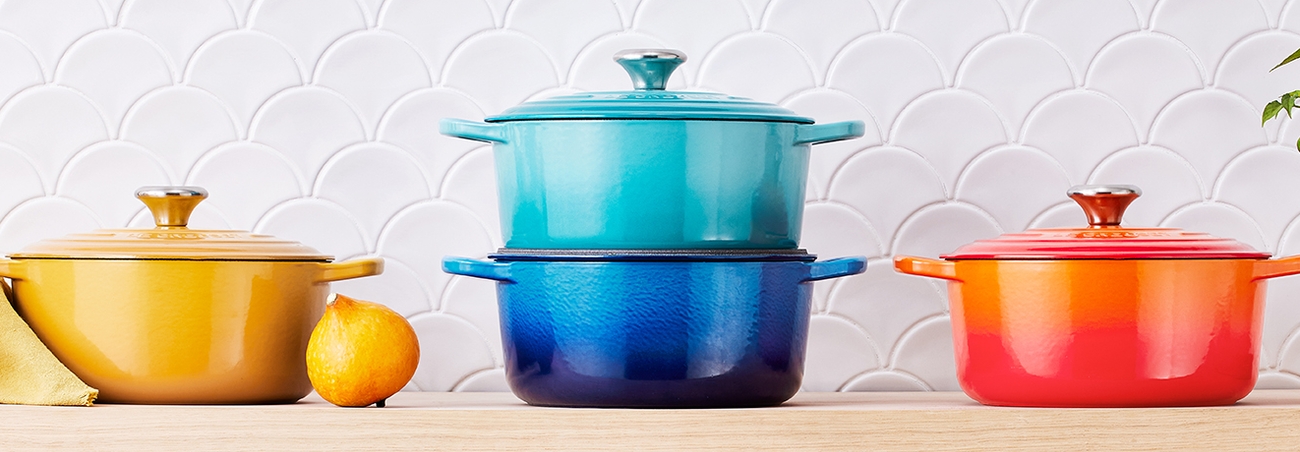 Le Creuset gjutjärnsgrytor i regnbågens alla färger på en hylla i ett kök