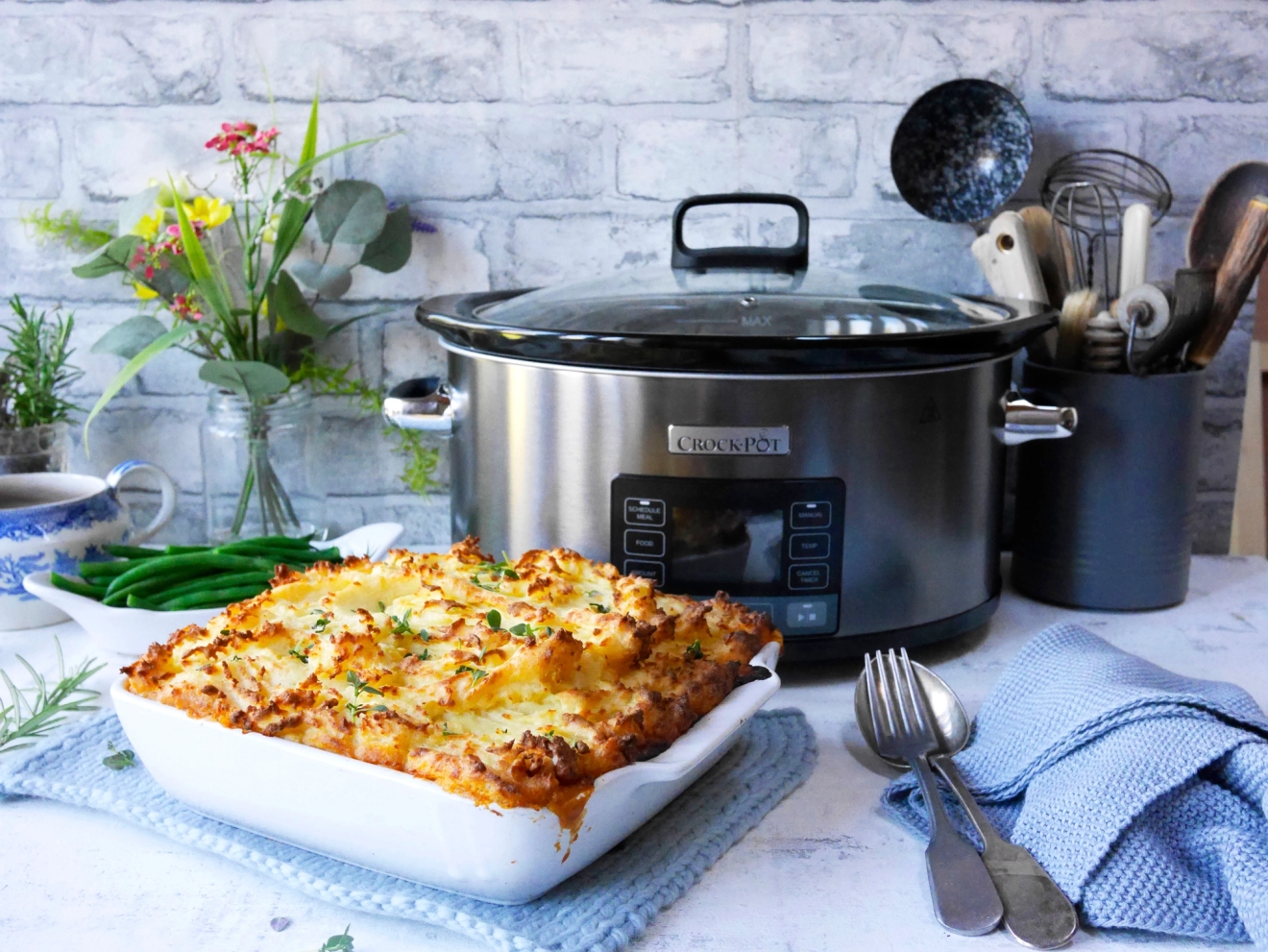 Uunissa gratinoitu vuokaruoka ja Crock-Pot-hidaskeittin aseteltuna keittiön pöydälle rustiikkisessa ympäristössä.