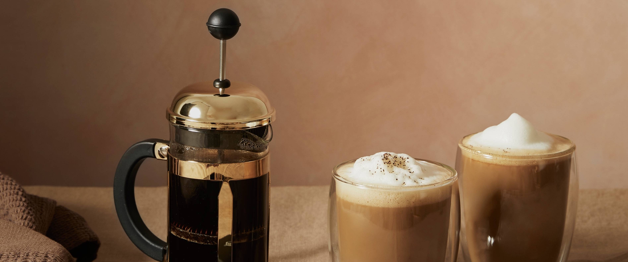 Presskanne i gull med kaffe og skummet melk i glasskopper