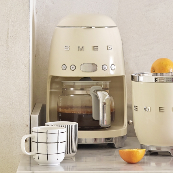 Smeg kaffebryggare beige med kaffe i med två kaffekoppar på bänk