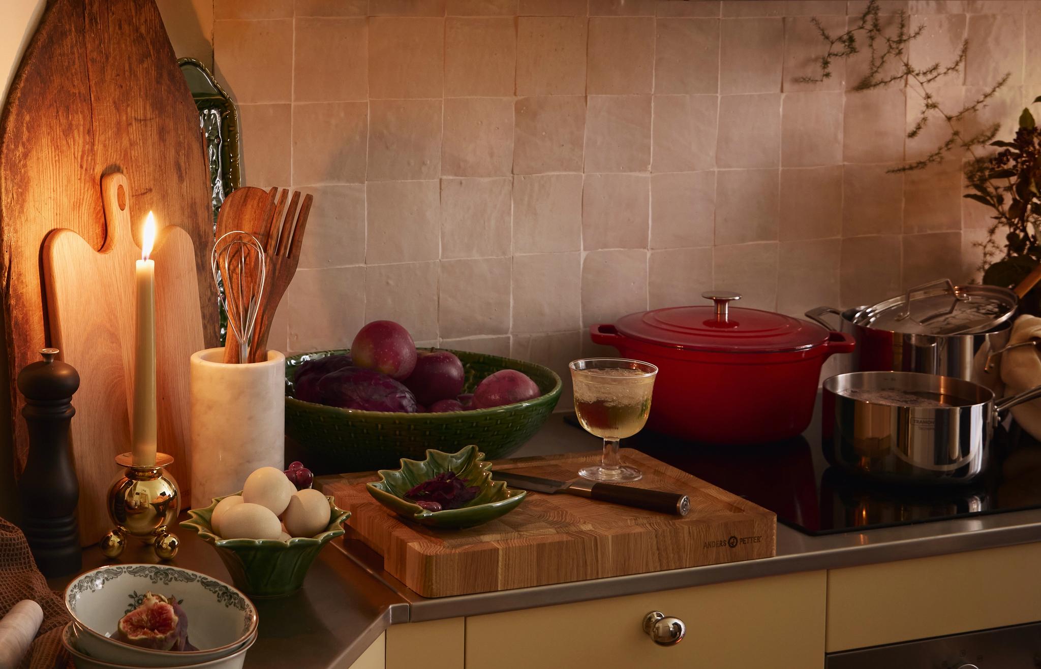 En mysig köksscen med ett tänt ljus, frukt, ägg, köksredskap och en ugnsbakning.