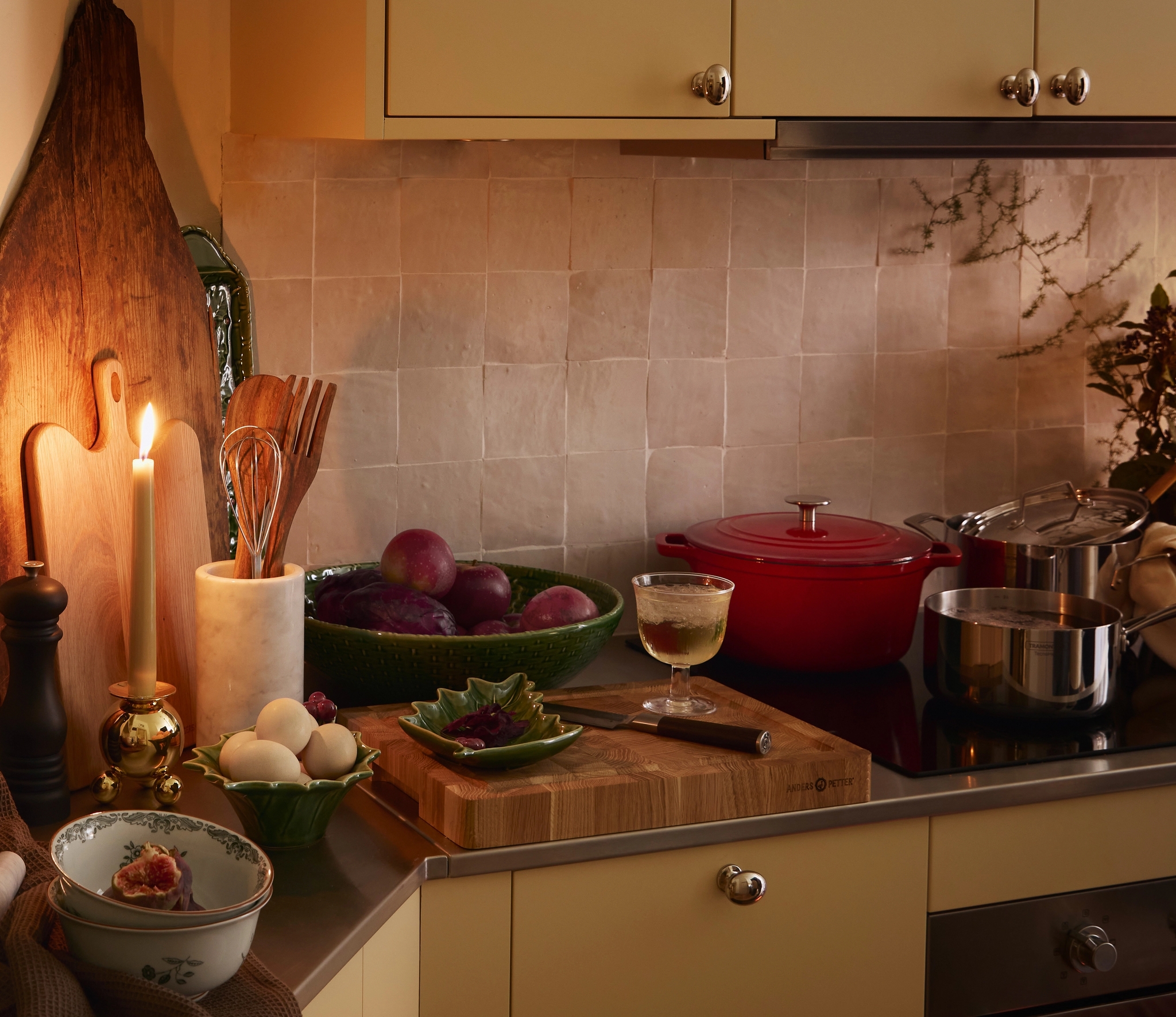 En mysig köksscen med ett tänt ljus, frukt, ägg, köksredskap och en ugnsbakning.