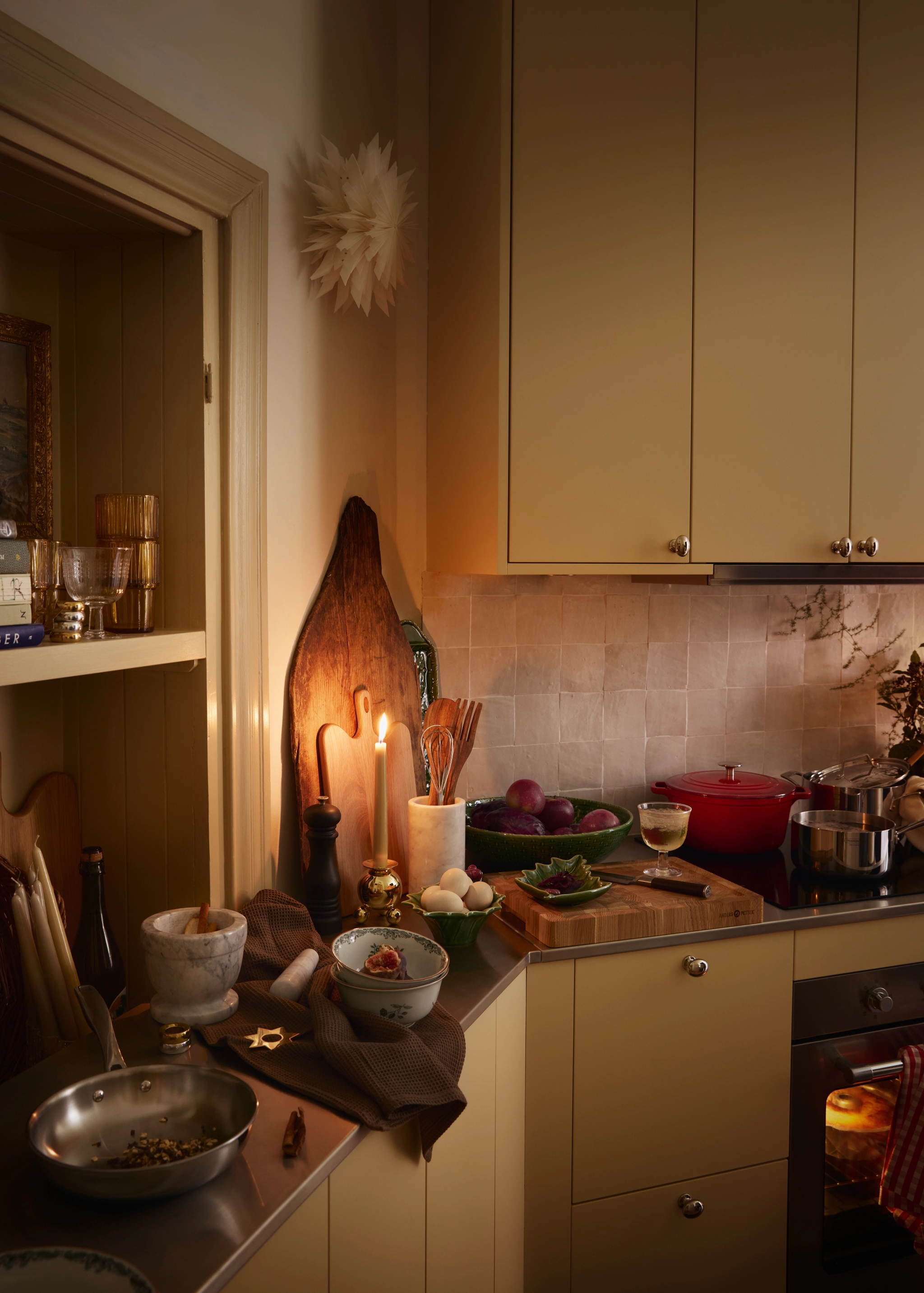 Lämmin, kynttilänvalossa hehkuva keittiötaso, jossa on ruoanlaittoaineksia, kattiloita ja hohkaava uuni.